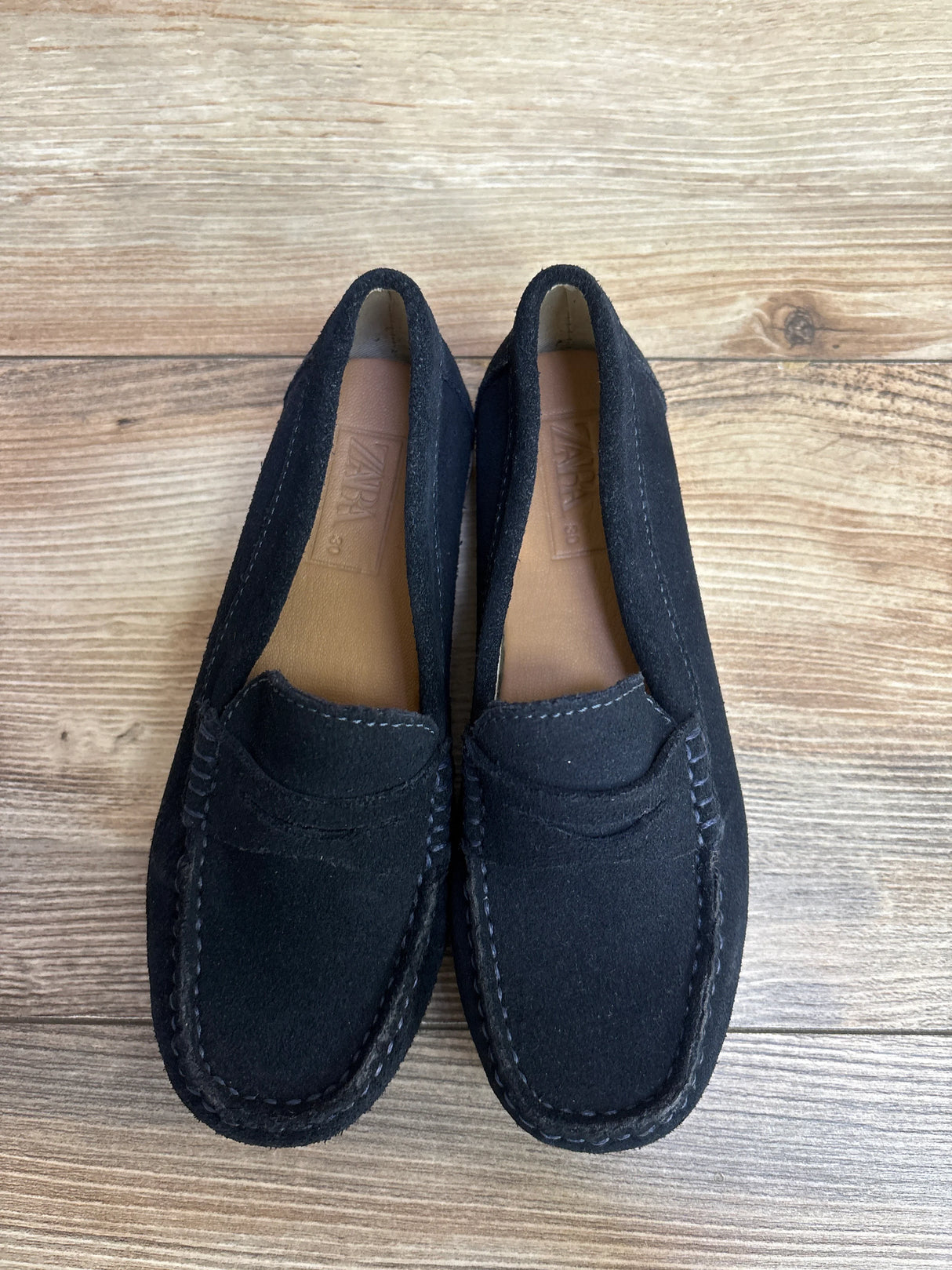 Black suede loafers with stitching on wood floor, Zara brand shoes