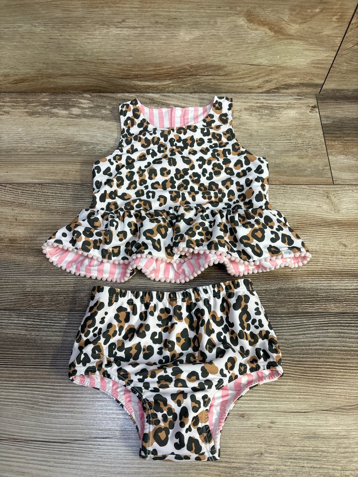Top down view of Mudpie reversible two piece swimsuit set with leopard print, pink striped reverse, and pom trimmed peplum