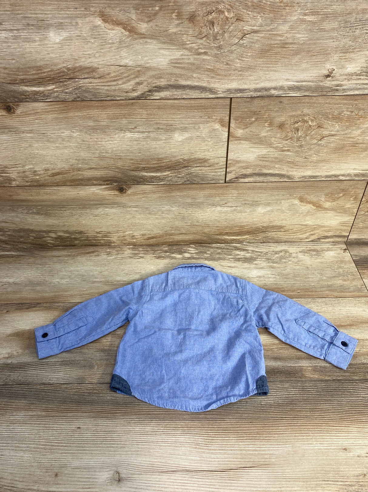 Blue long sleeve toddler shirt on wood background, back view, kids clothing flat lay