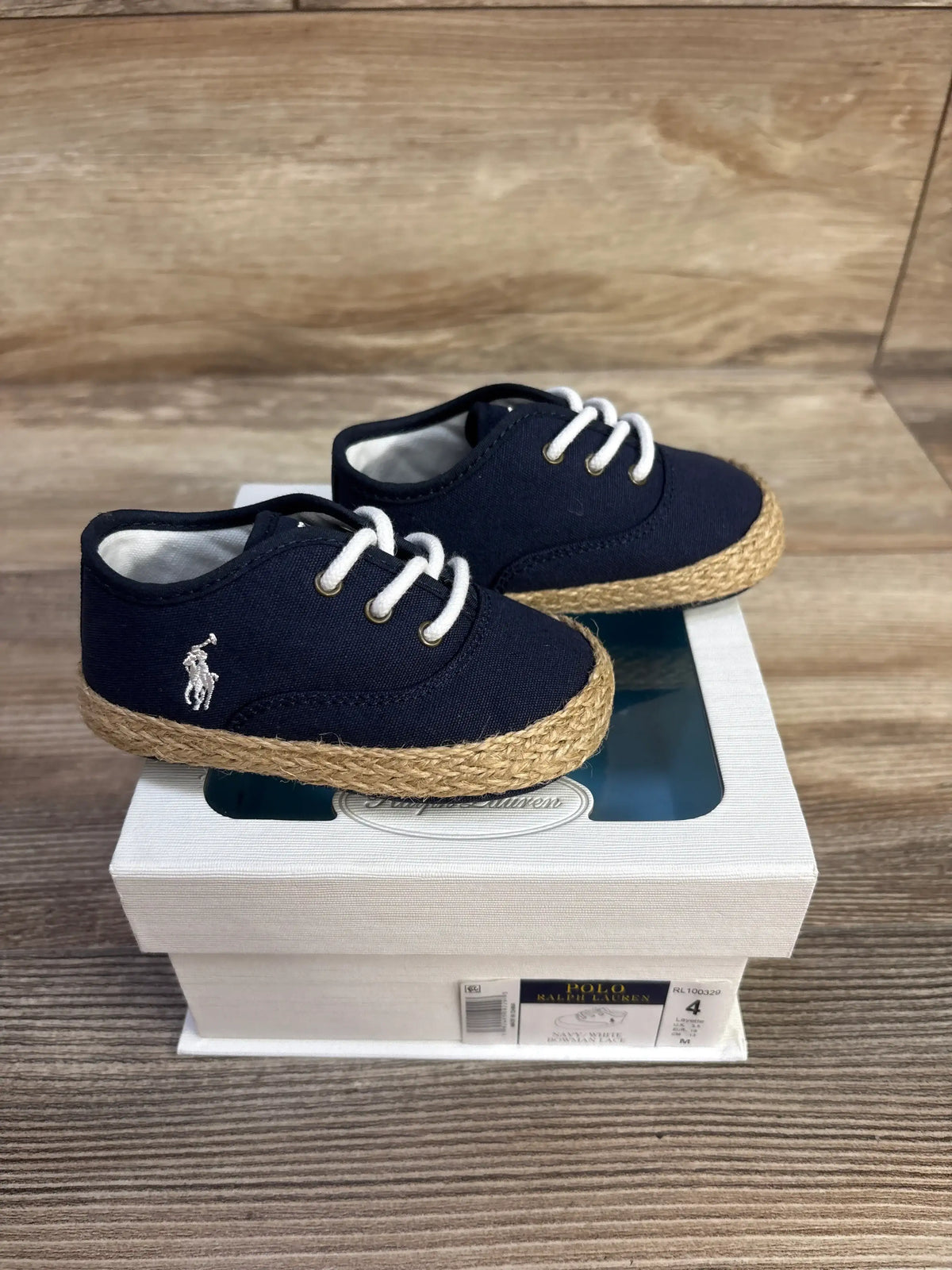 Front three-quarter view of navy Ralph Lauren Bowman crib shoes with white laces and braided soles on a display box