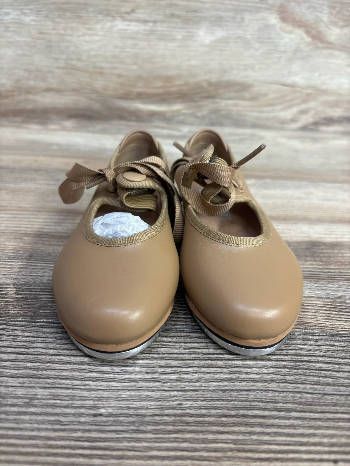 Tan children's tap dance shoes with ribbon laces on a wooden background