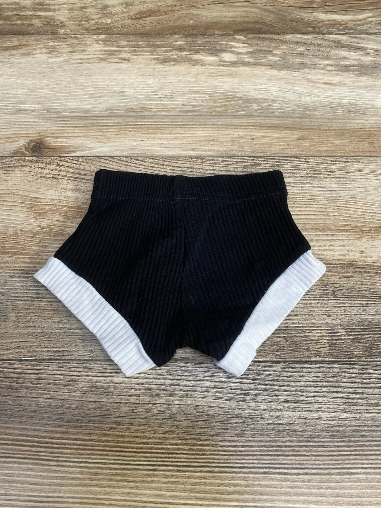 Top-down view of black ribbed baby bloomers with white cuffed legs on light wood background