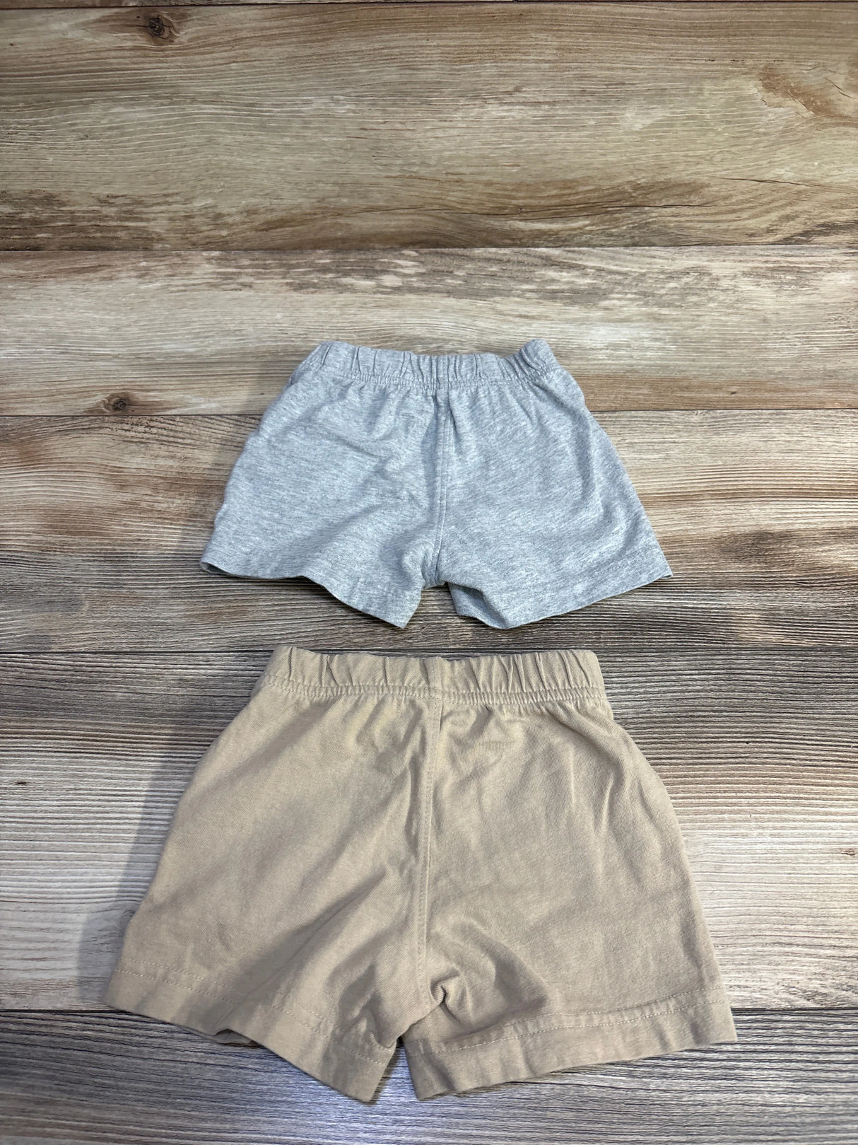Top-down view of two Baby Gap pull-on baby shorts, grey and beige, showcasing elastic waistbands on wood background