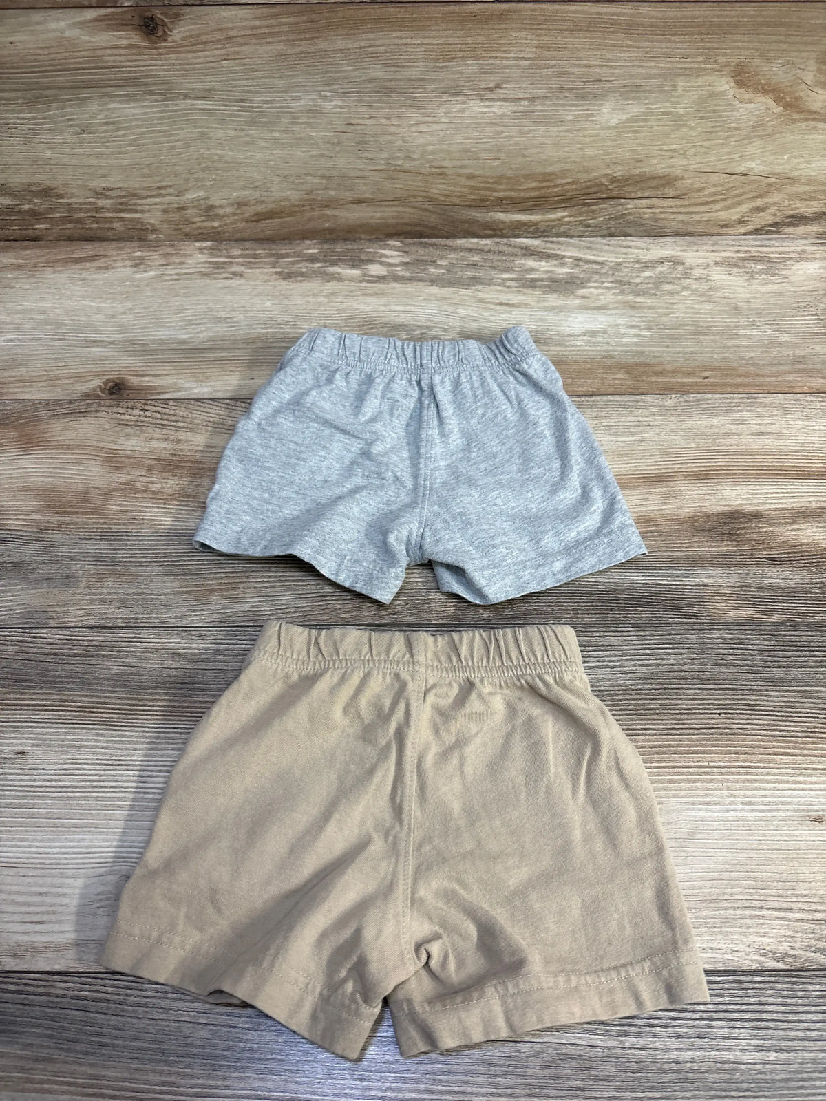Top-down view of two Baby Gap pull-on baby shorts, grey and beige, showcasing elastic waistbands on wood background