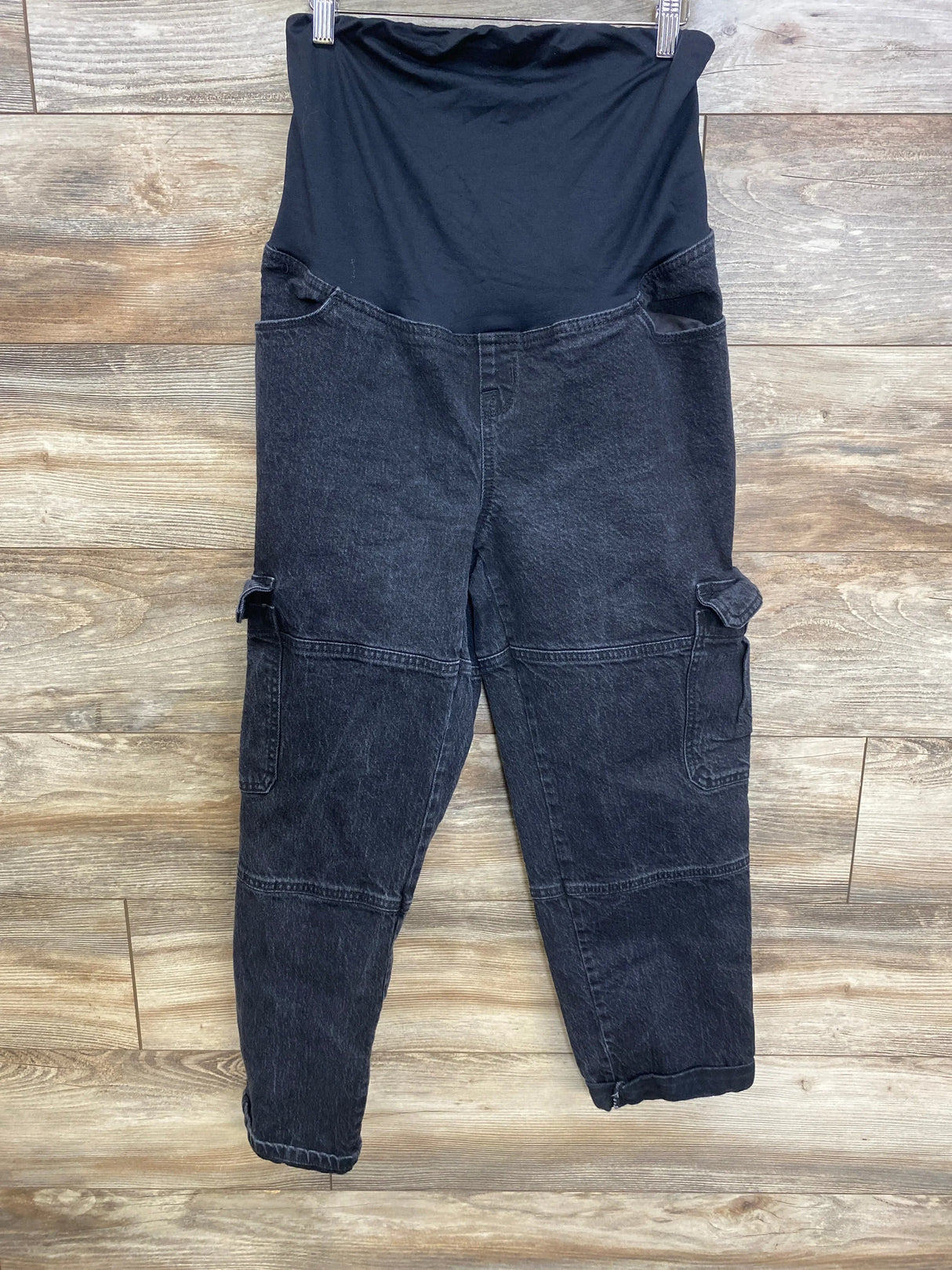 Front view of maternity 90s straight cargo jeans in black with stretch maternity panel and side cargo pockets on wood