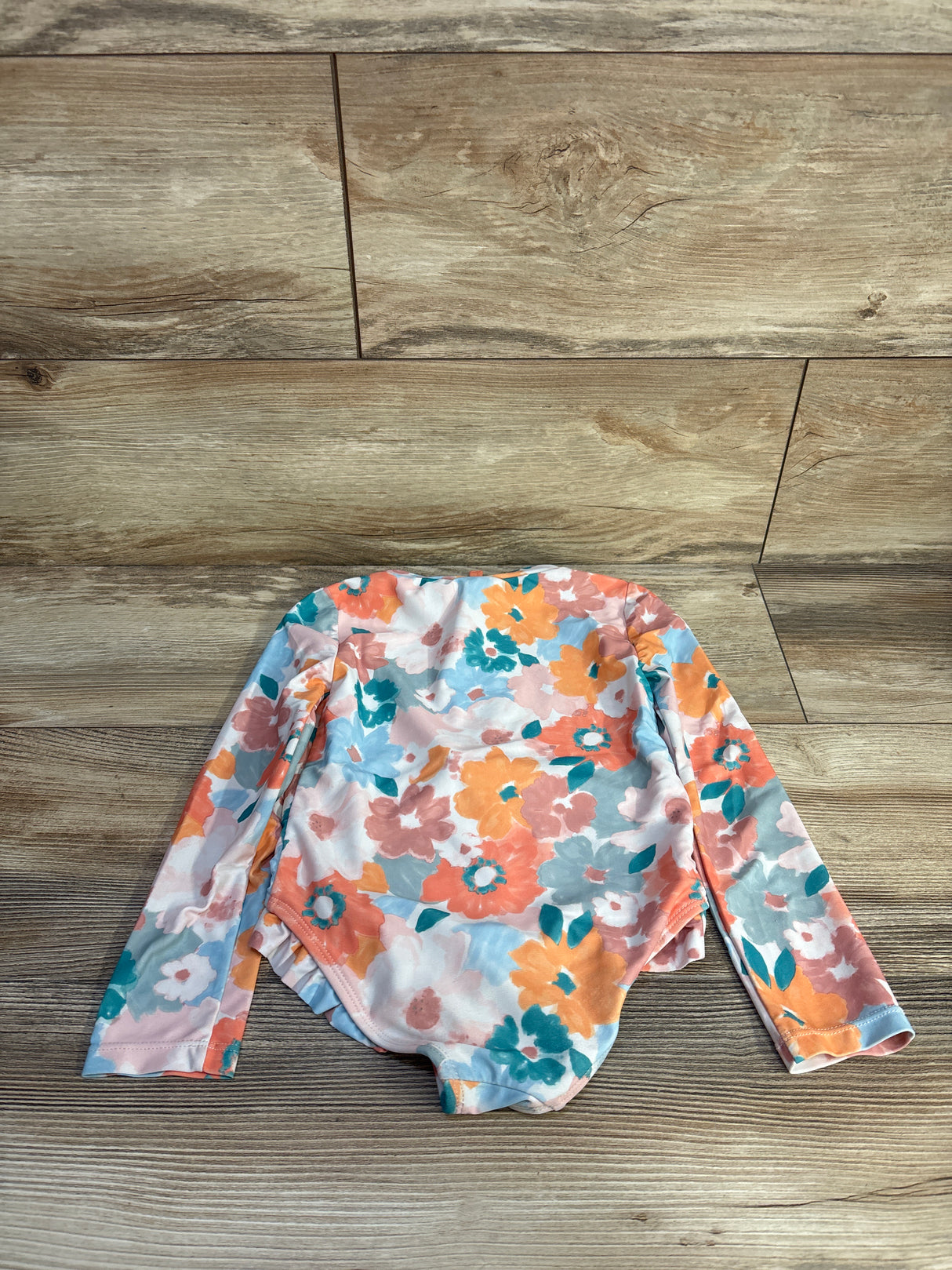 Flat-lay of multicolor watercolor floral long-sleeve rashguard swimsuit size 4T showcasing full front on wood background