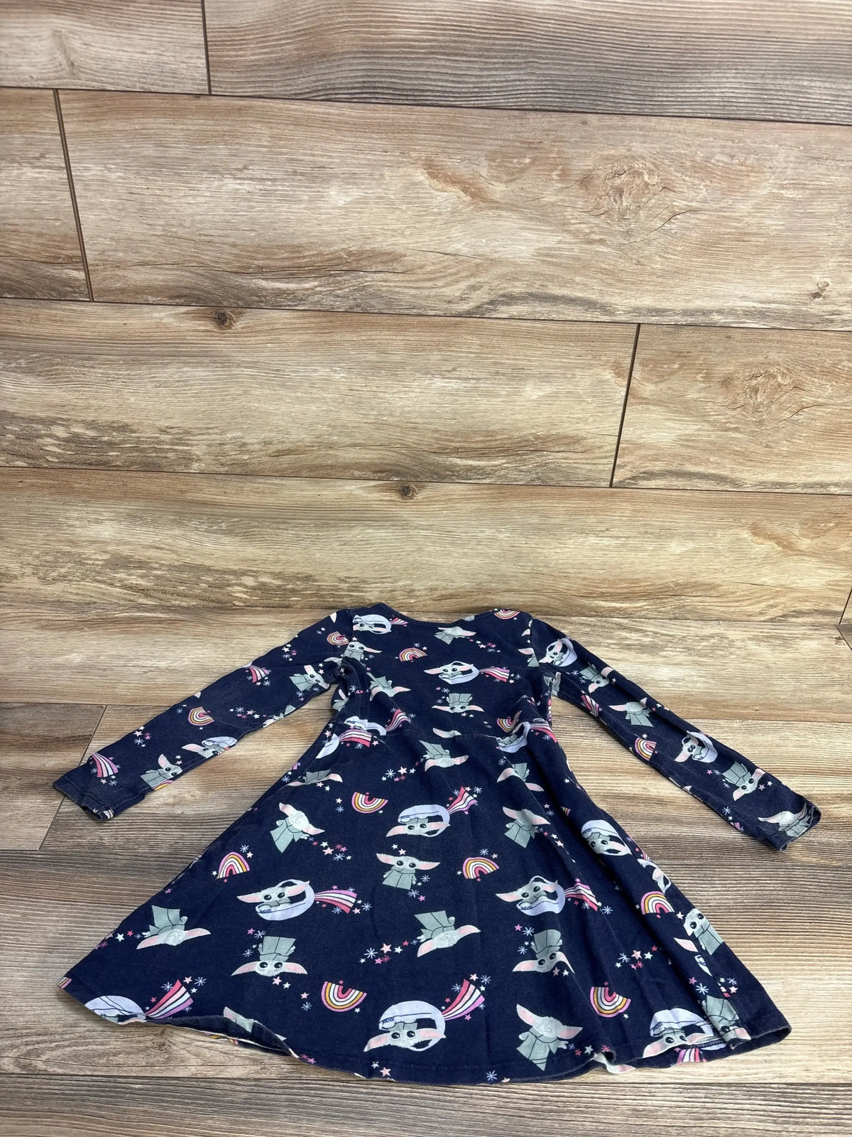 Flat lay of Jumping Beans x Star Wars Grogu navy dress showing long sleeves and Grogu rainbow print on wood floor background