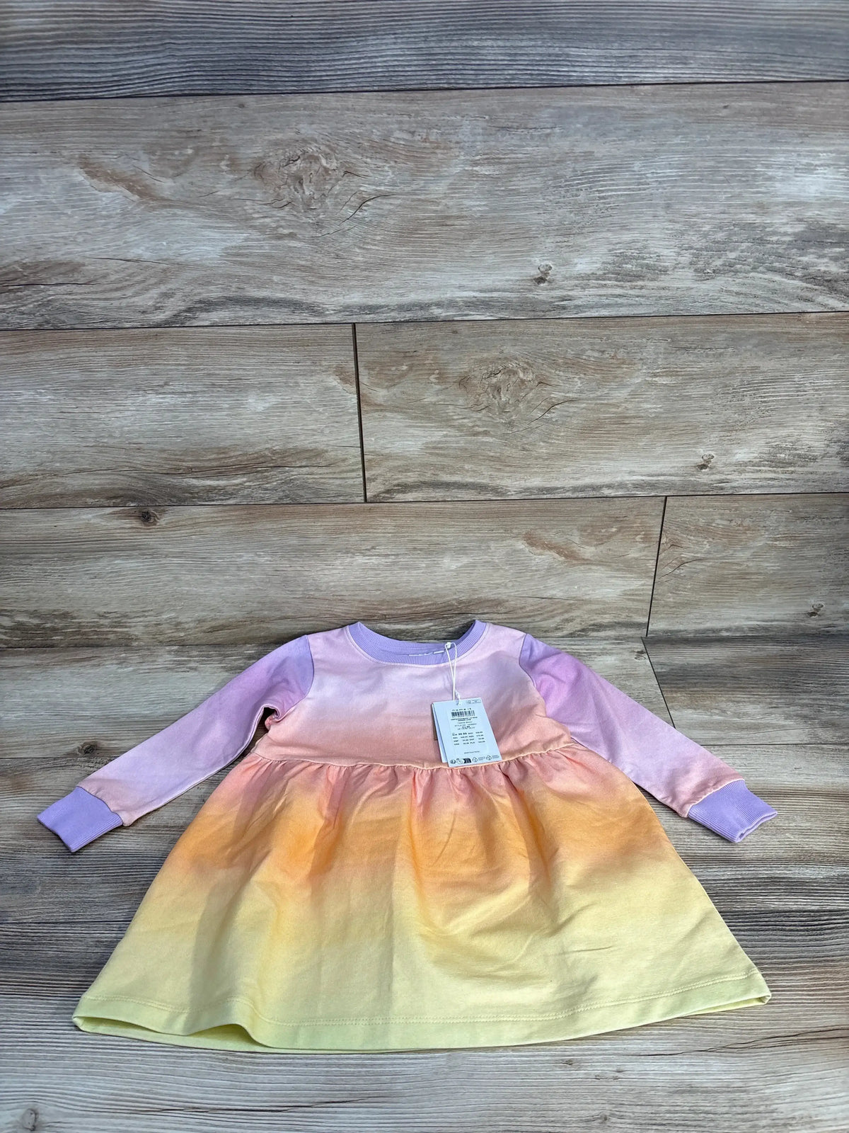 Flat lay of Name It rainbow long-sleeve dress size 2T showing pastel ombre skirt, purple sleeves, tag on wood floor