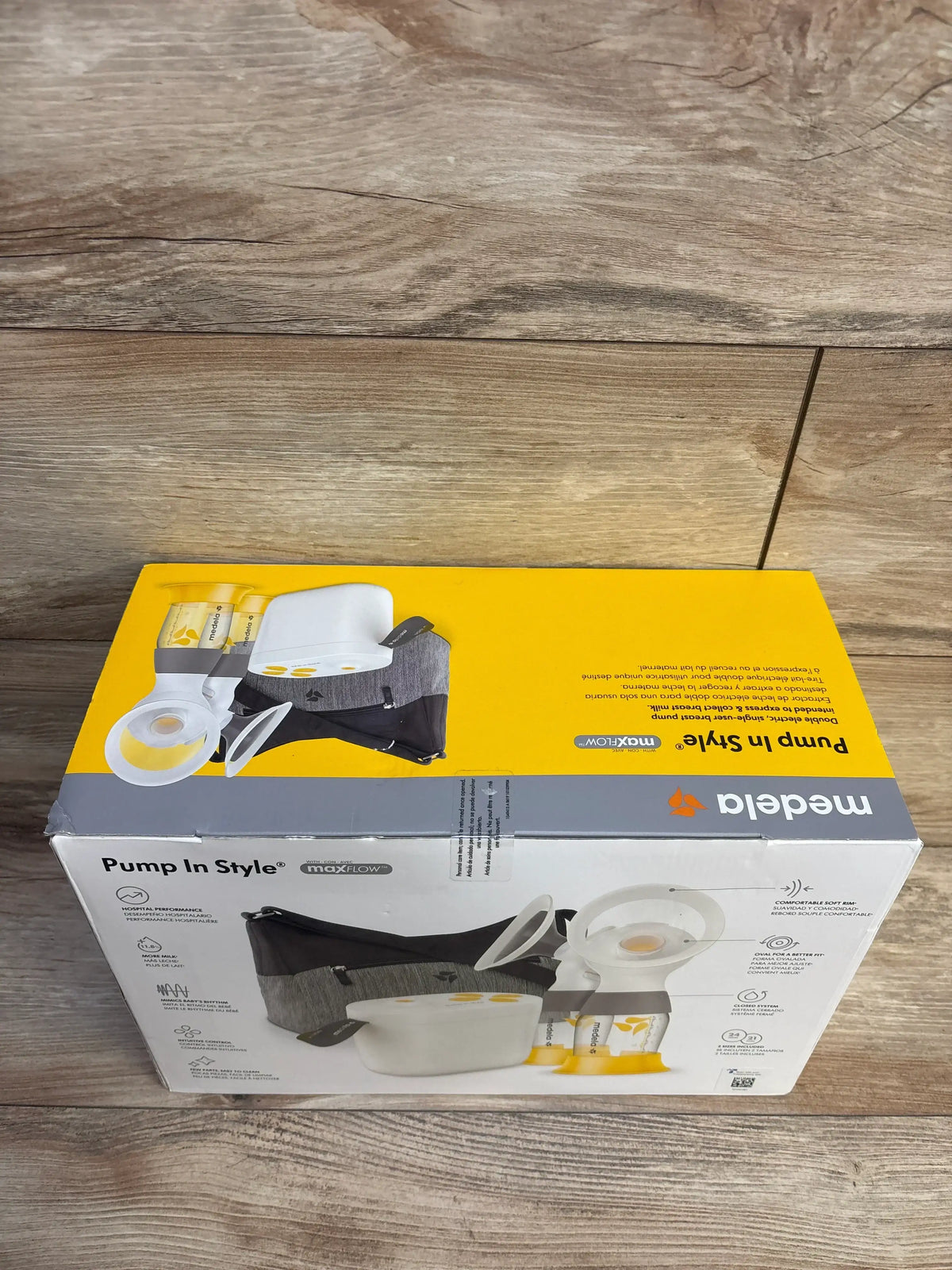 Angled top view of Medela Pump In Style with MaxFlow double electric breast pump box showing pictured pump parts and carrying bag on wood floor
