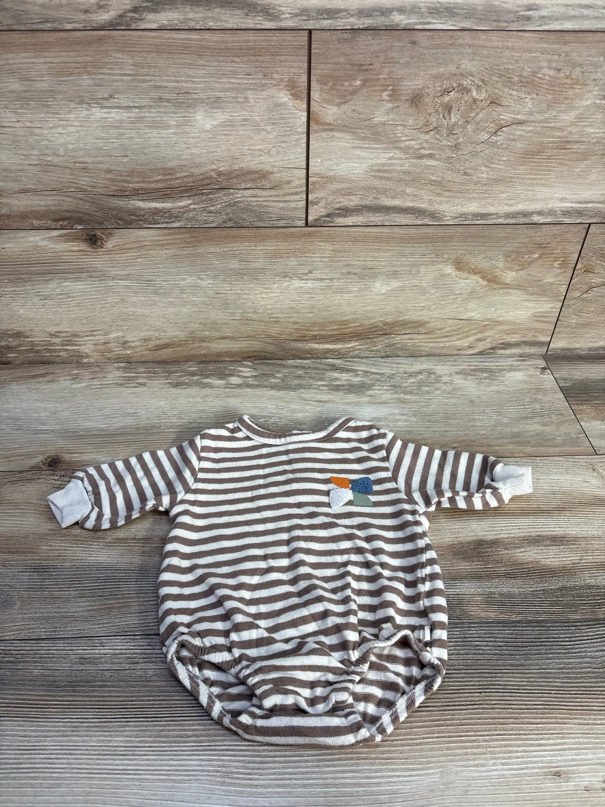Front view of Easy Peasy striped sweatshirt bubble romper in beige with long sleeves on a wood-grain background