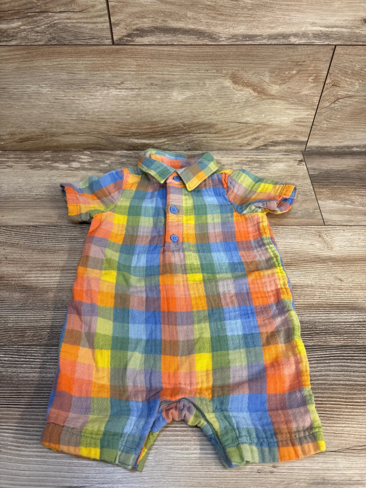 Colorful plaid baby romper with short sleeves and blue buttons, laid on wood floor