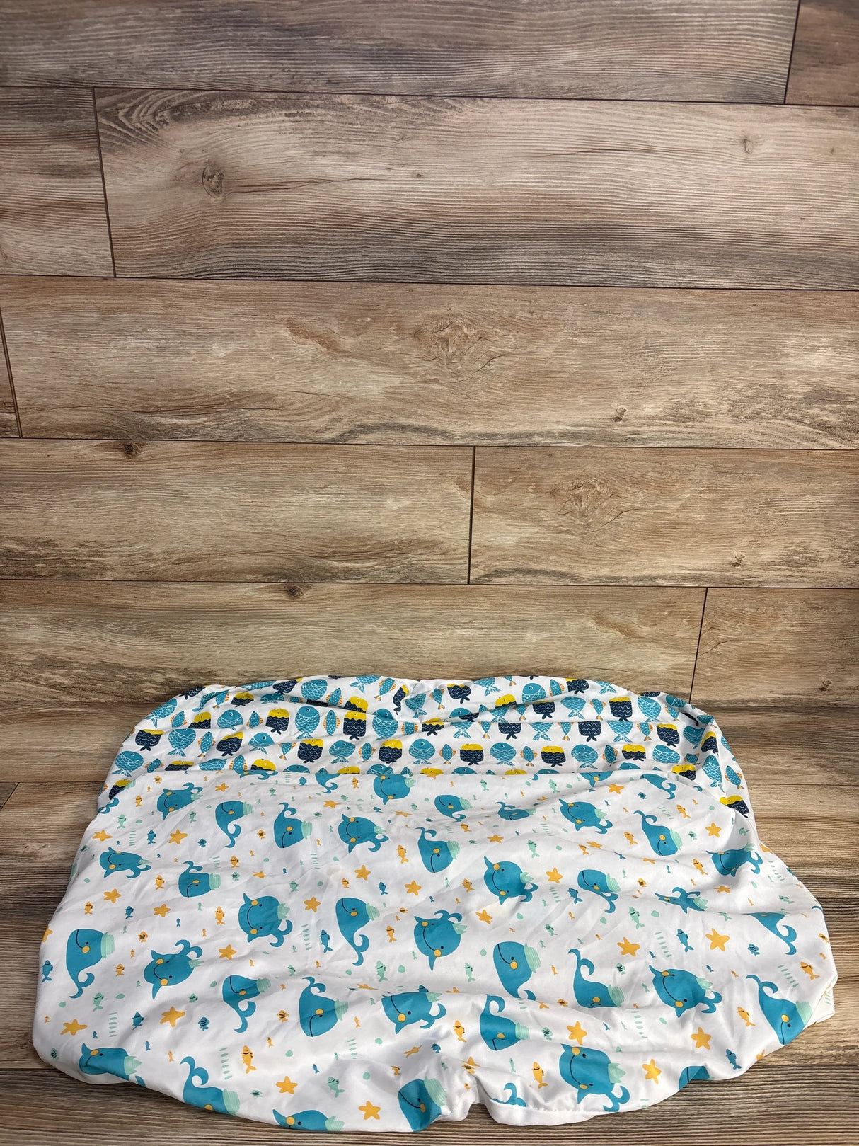 Blue and yellow whale and fish patterned baby changing pad on wooden floor