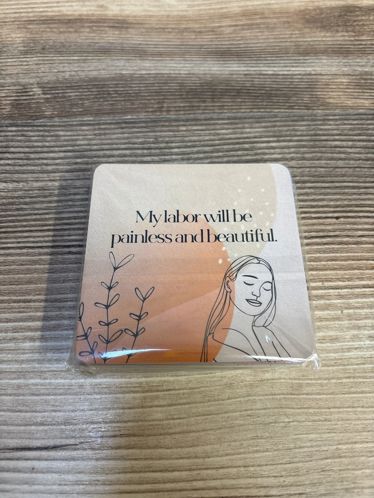 Affirmation card with illustrated woman and text 'My labor will be painless and beautiful' on wood surface