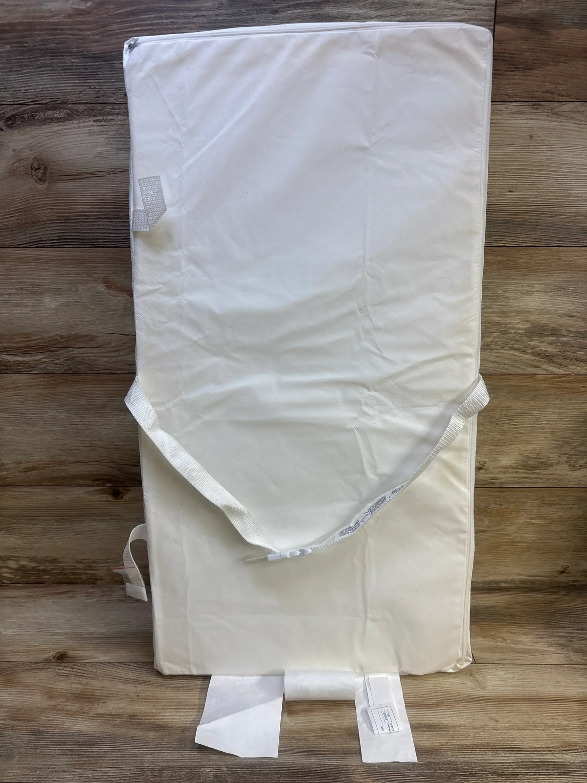Top view of a Delta Children foam contoured changing pad showcasing its white cover and contoured edges on a wood floor