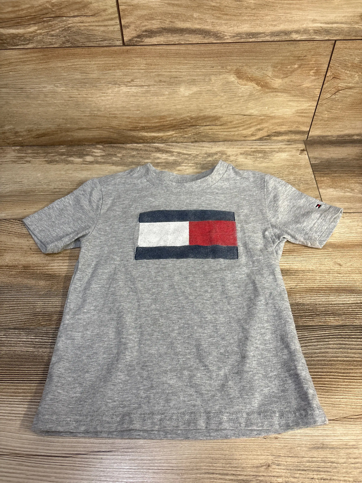 Front view of Tommy Hilfiger grey toddler shirt in size 3T showcasing chest flag logo with wood floor background