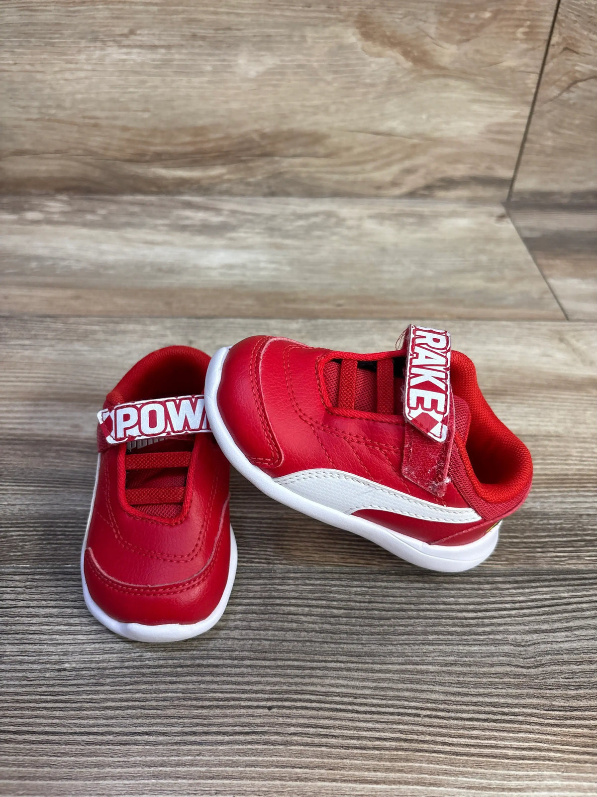 Front and side views of red Puma x Scuderia Ferrari Kart Cat III sneakers showing hook-and-loop straps on wood flooring