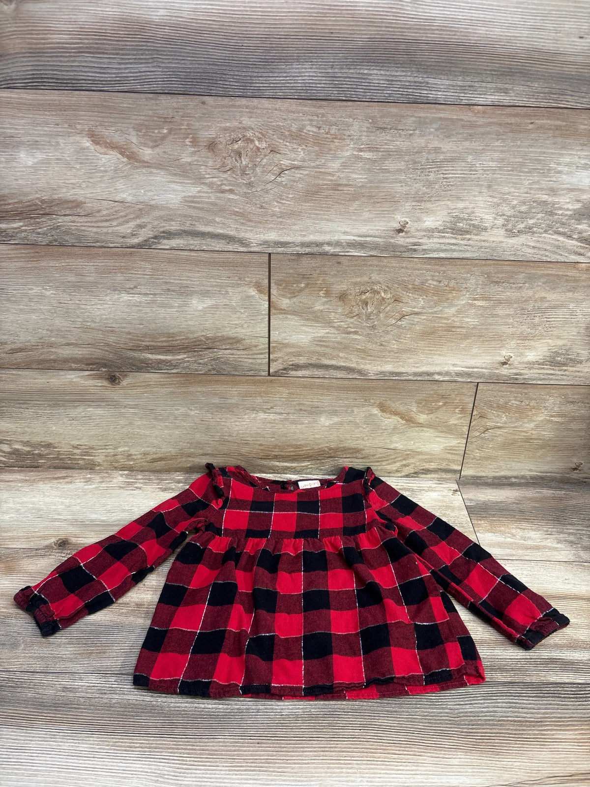 Front view of Jumping Beans red and black plaid flannel long sleeve top showcasing a ruffled yoke on a wood-look floor