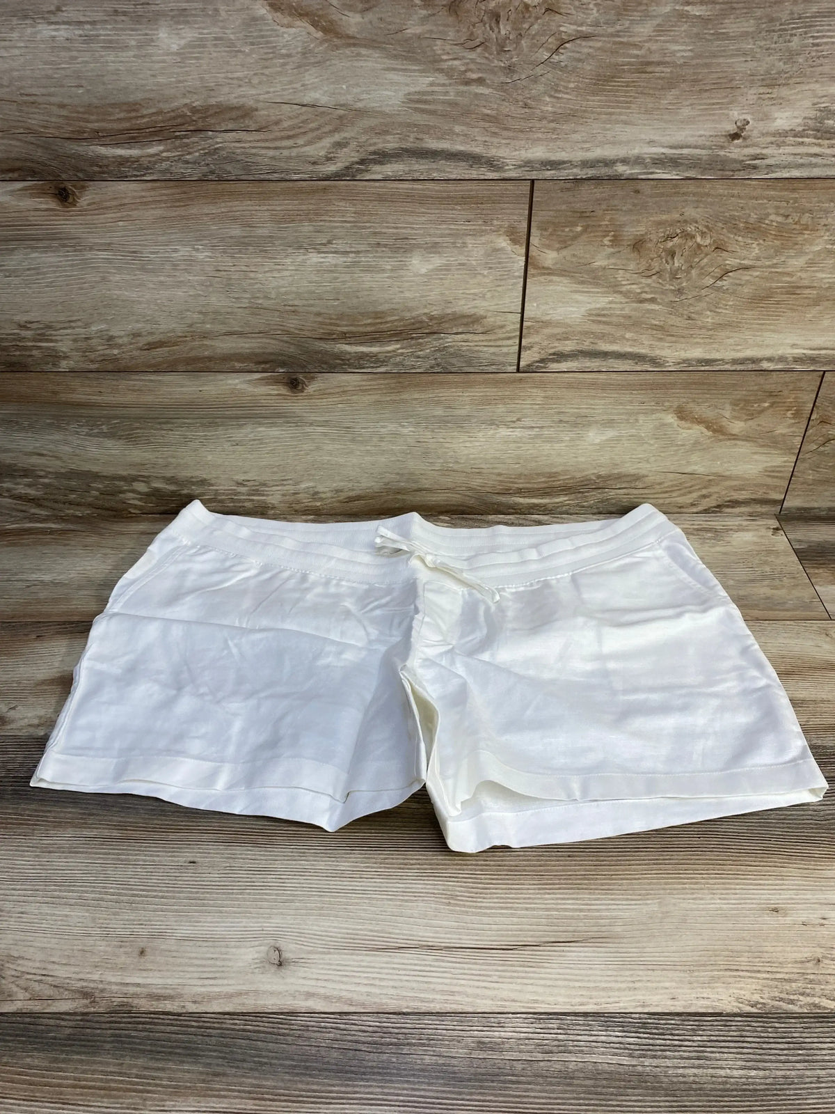 Front view of white Gap maternity linen-cotton shorts showcasing drawstring waist and roomy fit on light wood background