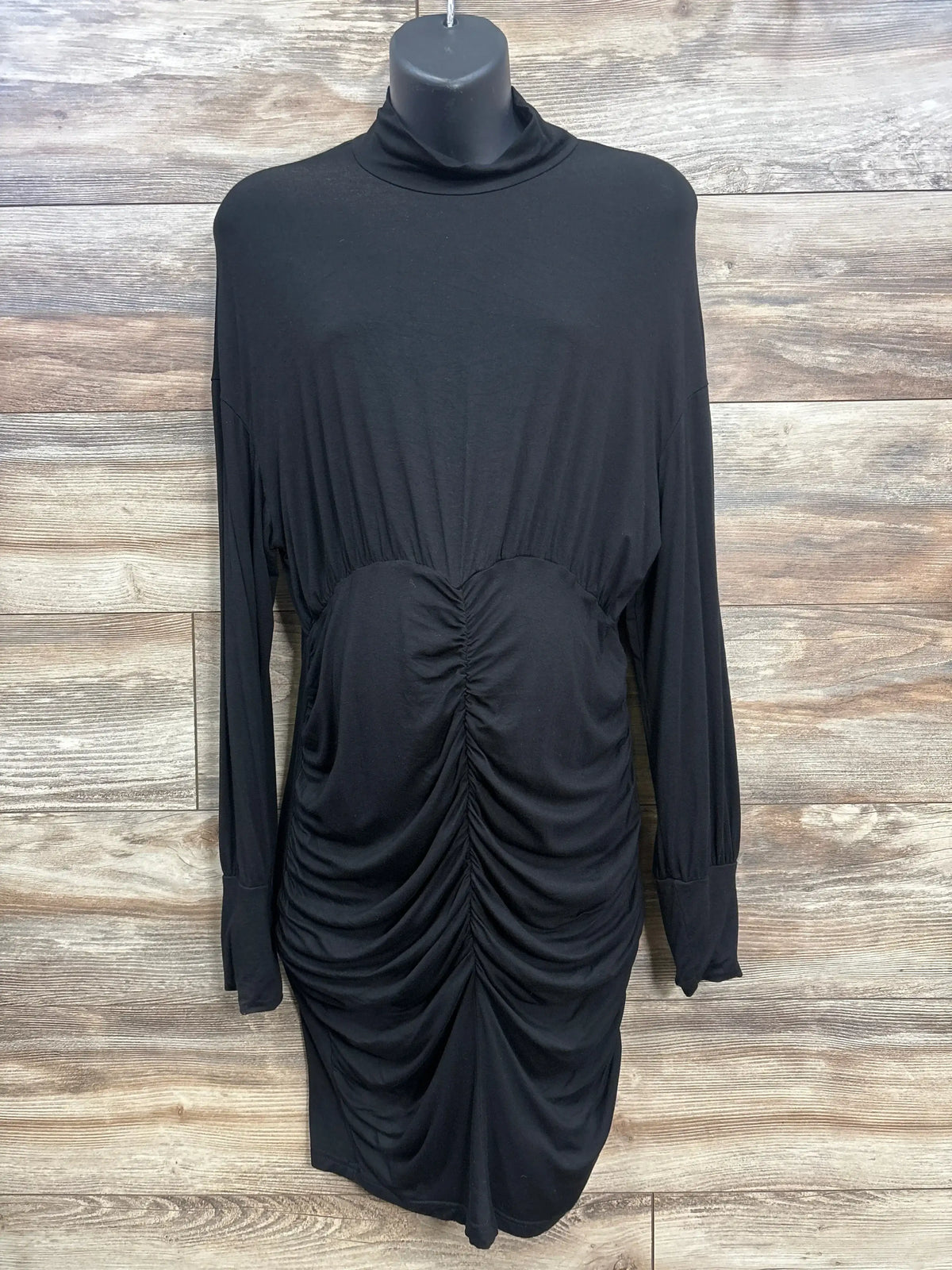 Black ruched maternity long sleeve dress with mock neck on hanger, wood background