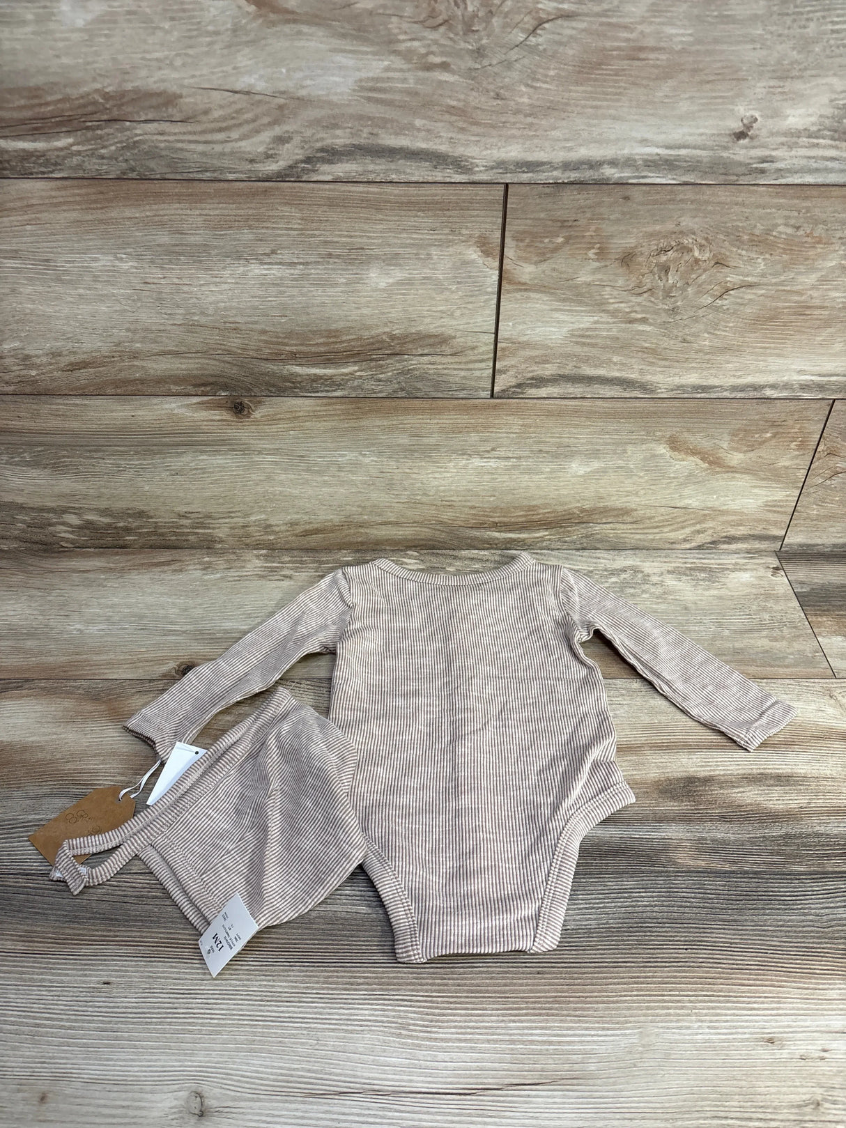 Top-down of taupe ribbed striped long-sleeve baby bodysuit and matching bonnet on wood background