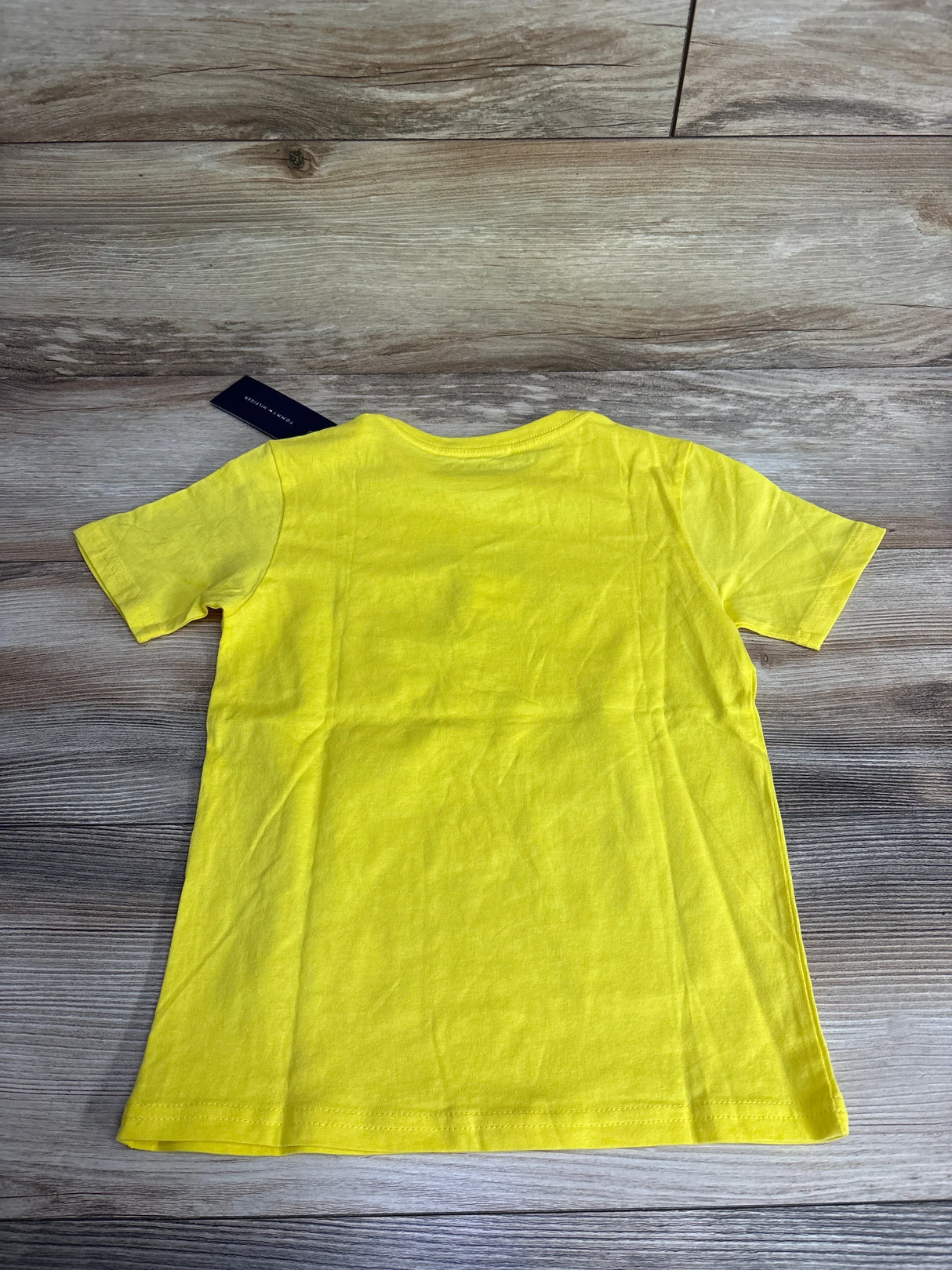 Bright yellow children's short-sleeve t-shirt laid flat on wood floor with Tommy Hilfiger tag