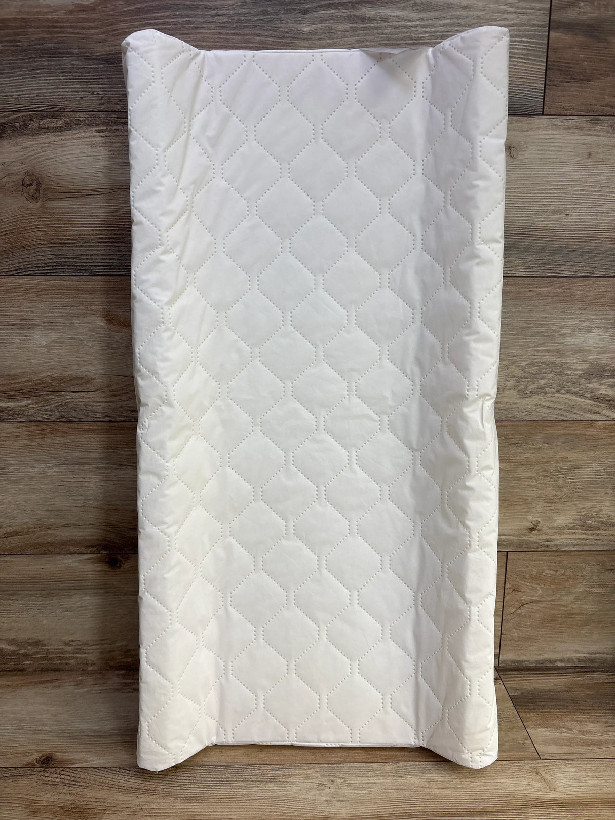 White quilted baby changing pad on wood floor, diamond pattern, kids nursery accessory