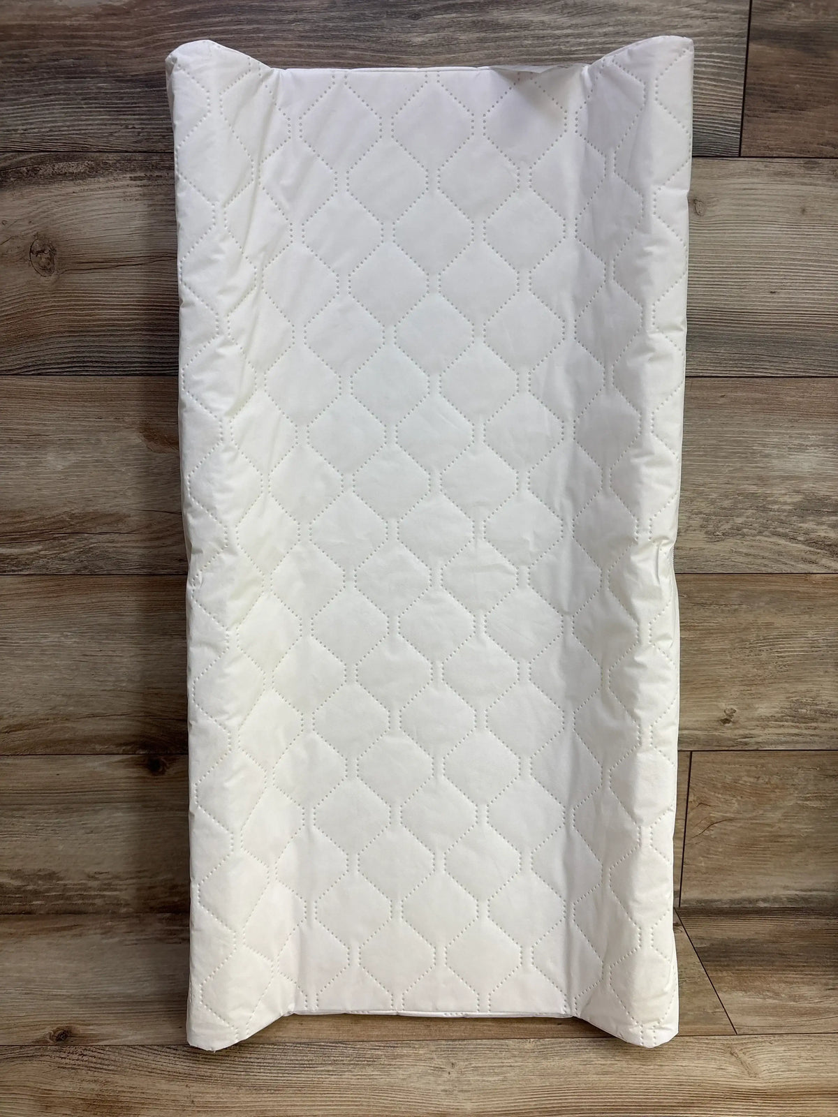 White quilted baby changing pad on wood floor, diamond pattern, kids nursery accessory