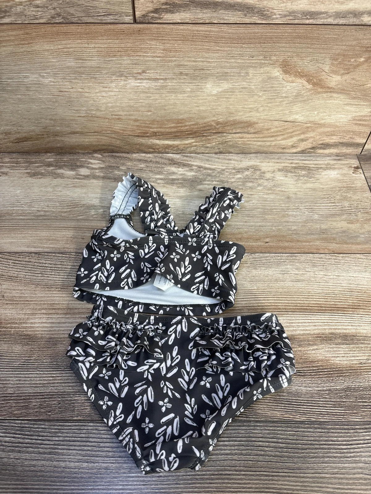 Carter's 2pc grey ruffle swimsuit set with white leaf print on a wooden background