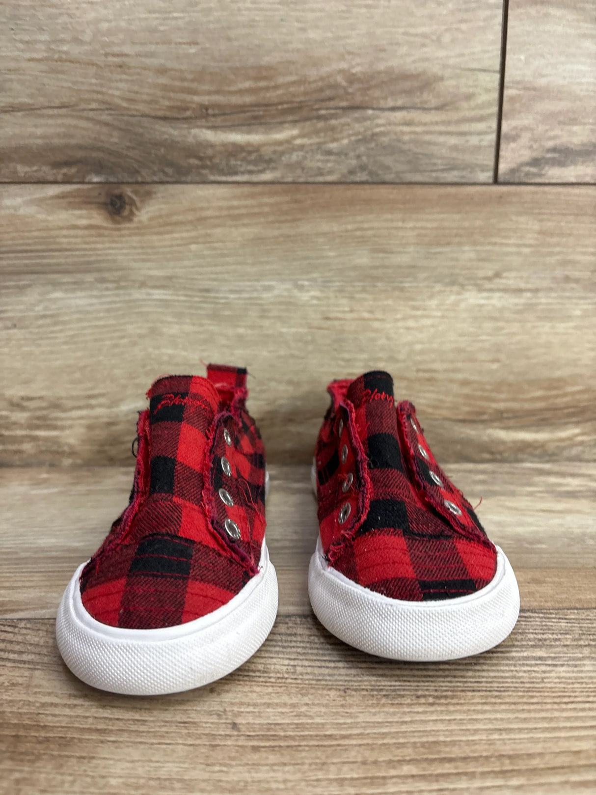 Red and black plaid toddler slip-on shoes with white soles on wooden floor