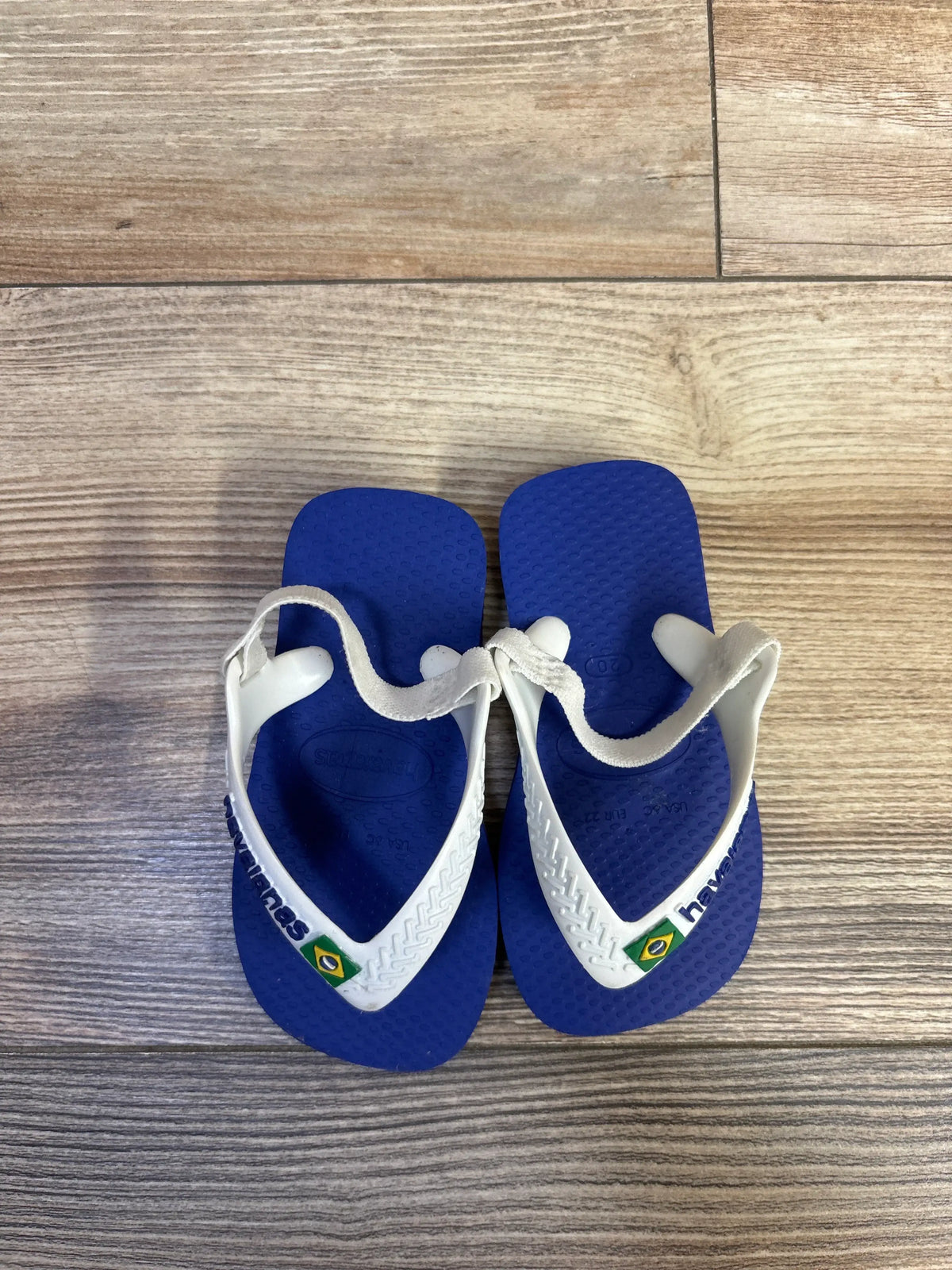 Top view of Havaianas blue thong flip flops, size 6C, showcasing elastic ankle straps on a wood floor