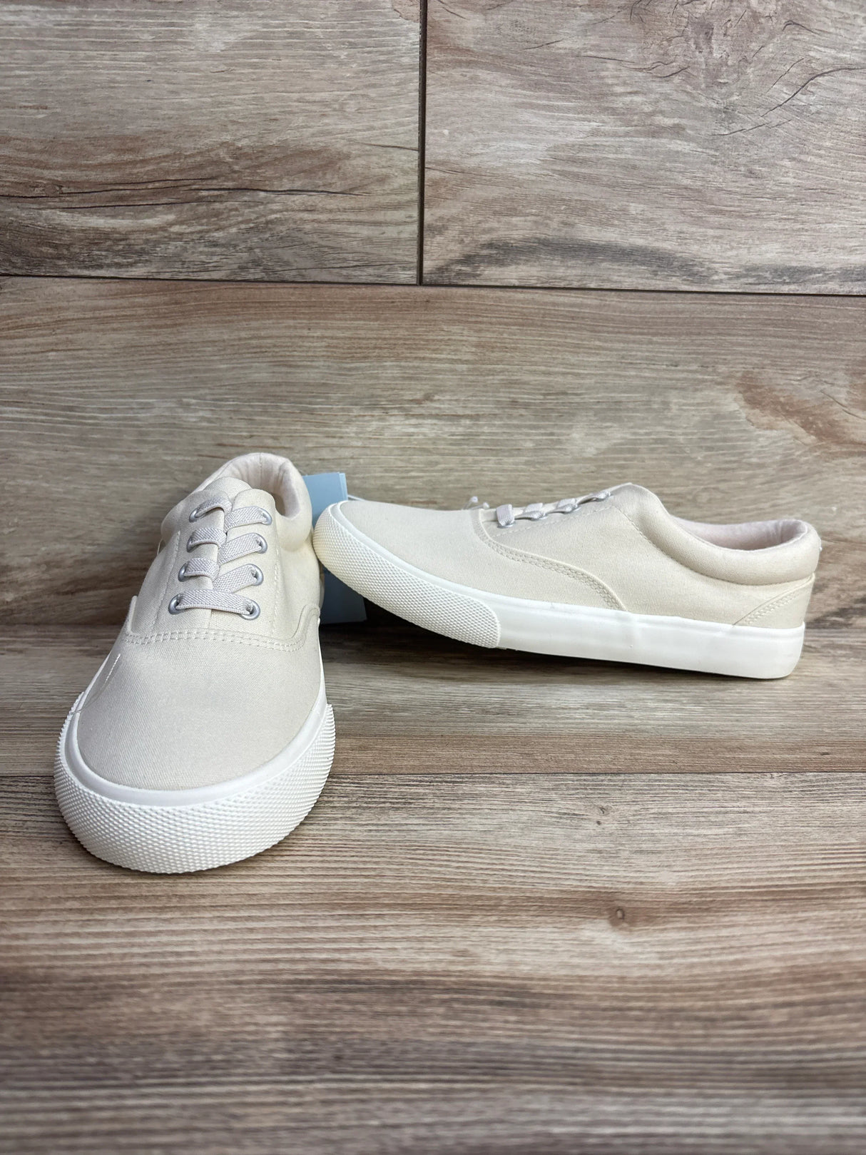 Beige canvas toddler sneakers with white rubber soles on wooden background