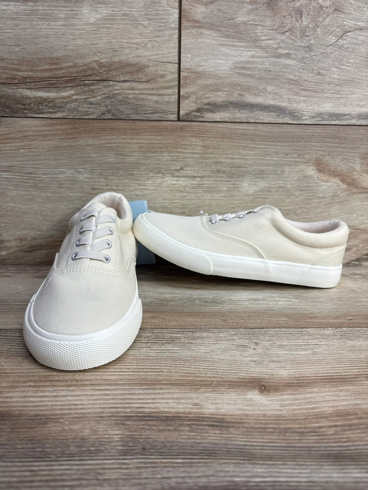 Front and side view of Cat and Jack Tyler slip-on sneakers showcasing off-white canvas uppers, elastic laces, and padded collars on a wood-look floor
