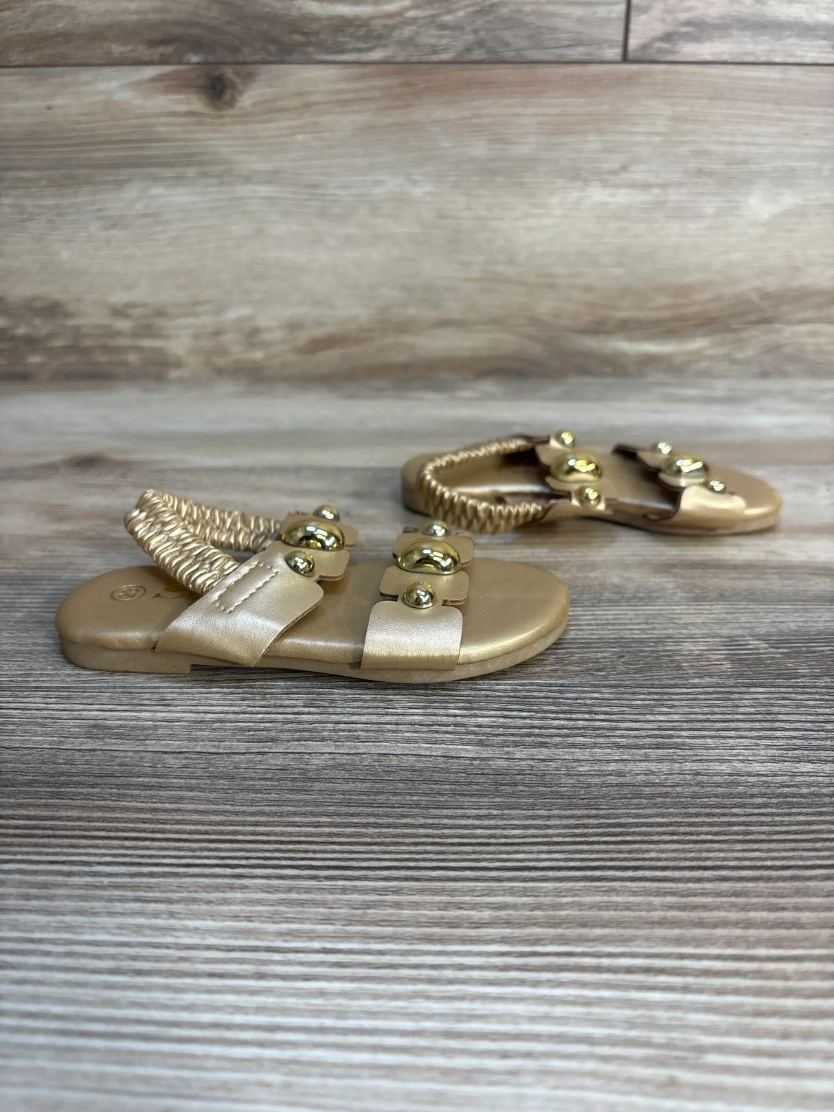 Gold toddler sandals with decorative flower accents on wooden surface