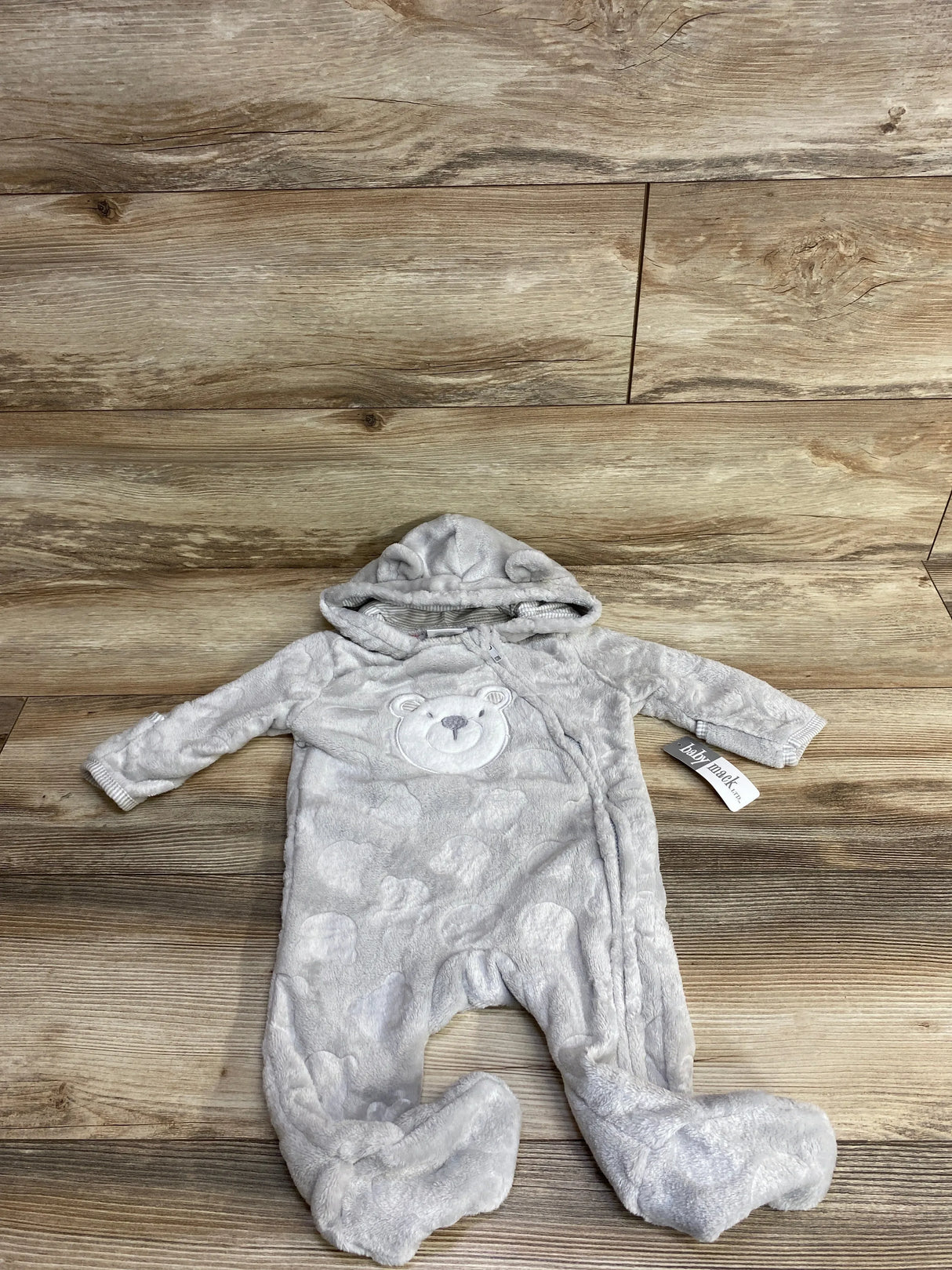 Gray plush baby onesie with hood and bear face design, lying flat on wood floor background