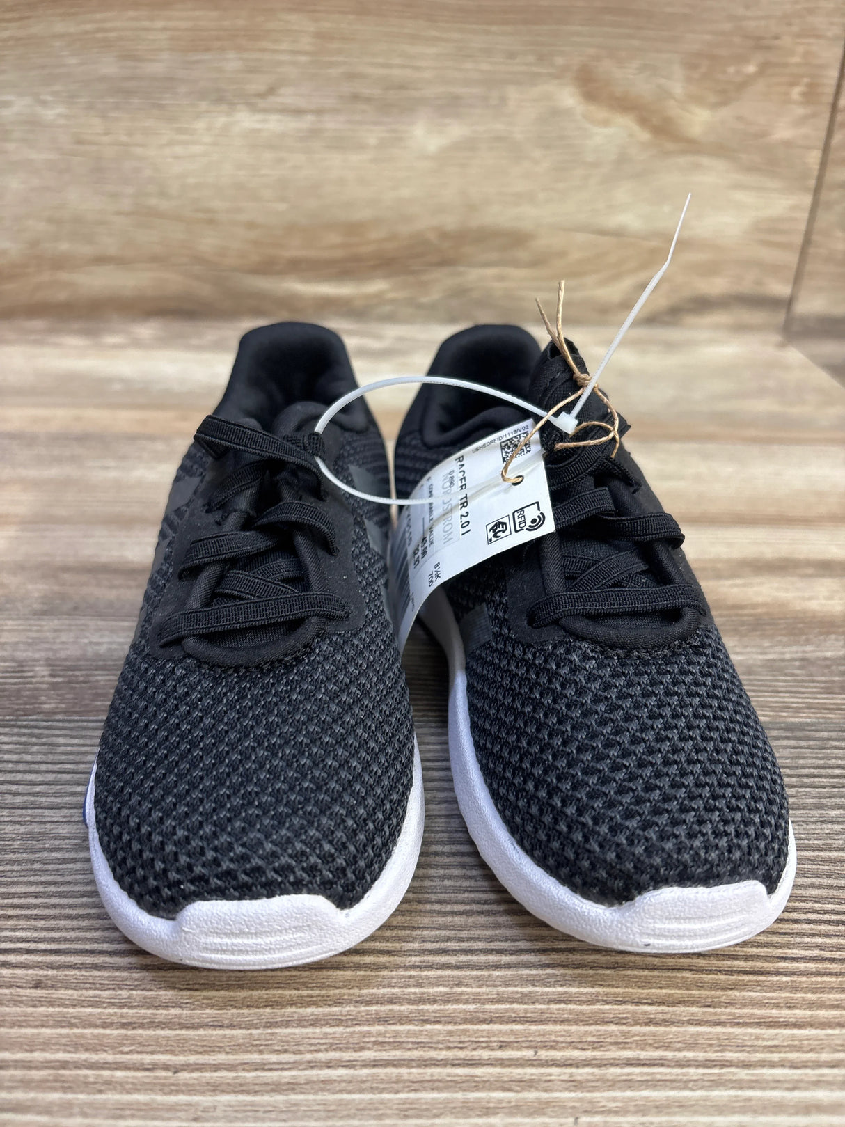 Front view of Adidas Racer TR 2.01 toddler sneakers in black showing knitted upper, white sole, laces and attached size 9C tag on wood surface