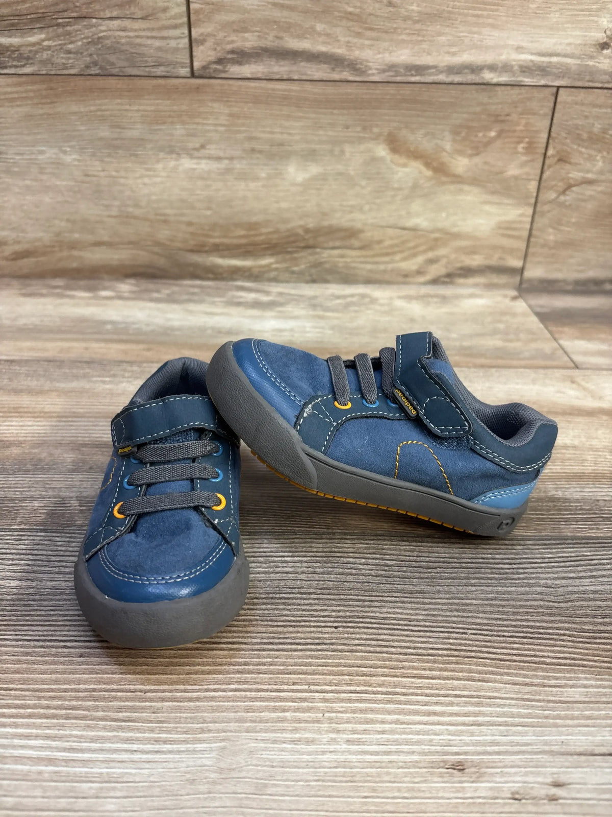 Front and side view of blue Pediped Dani-Flex sneakers showcasing straps, laces, and gray rubber soles on a wood floor