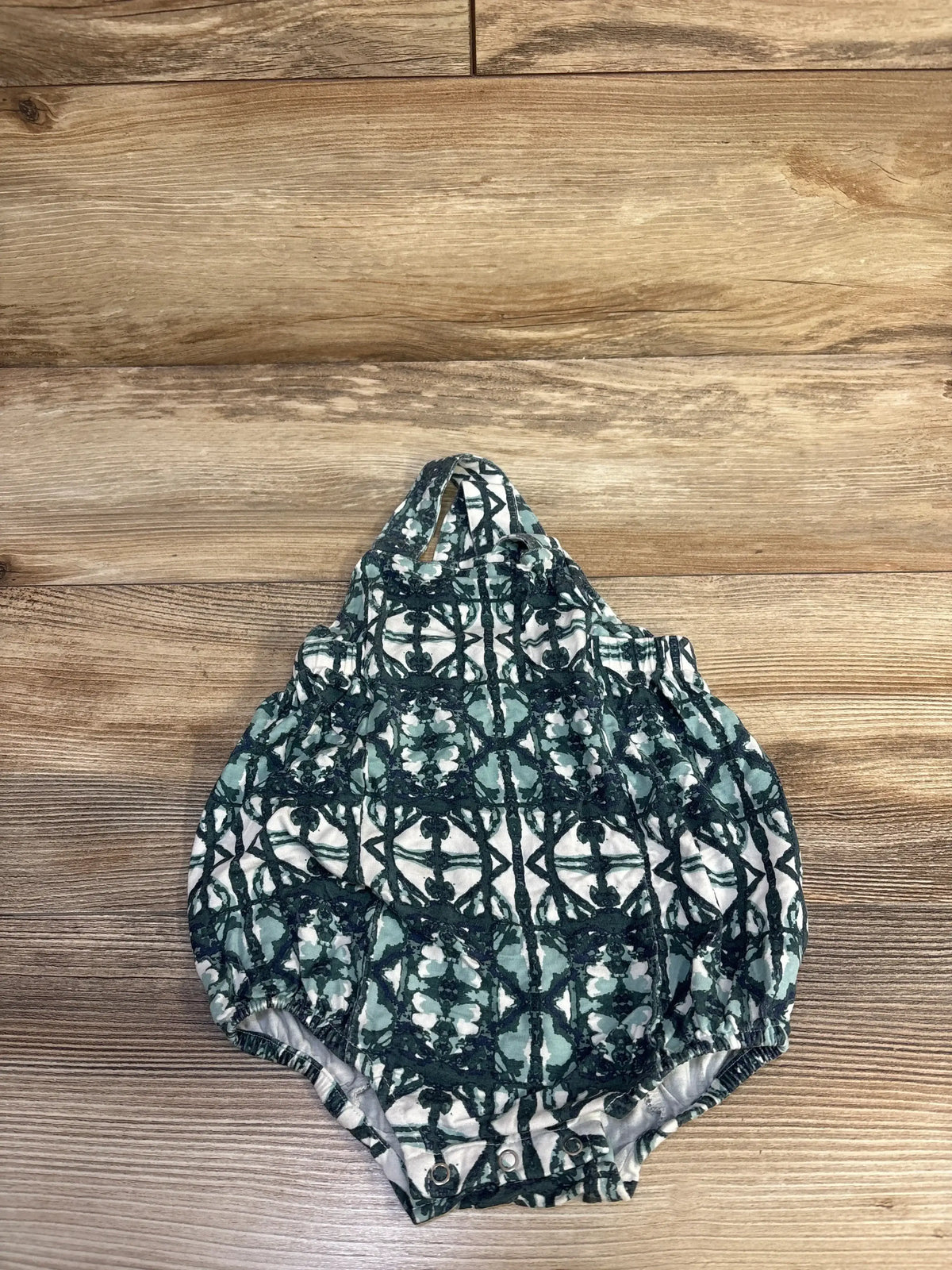 Front flat lay of sleeveless bubble romper showcasing green geometric print, elastic leg openings and snap crotch on wood plank background