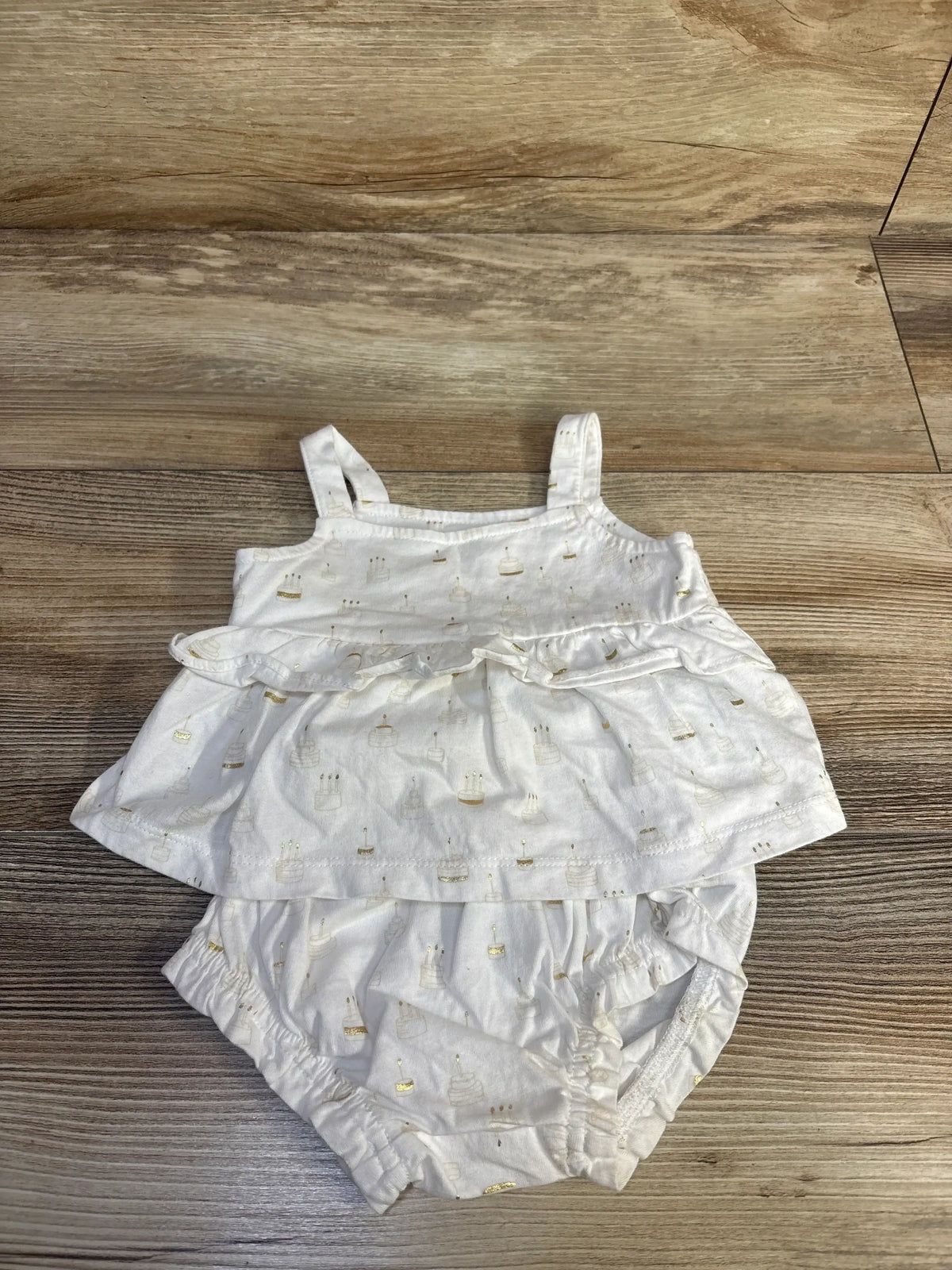 Top view of Baby Gap white 2pc Birthday Cake outfit ruffle tank and bloomers with gold cake print on wood floor