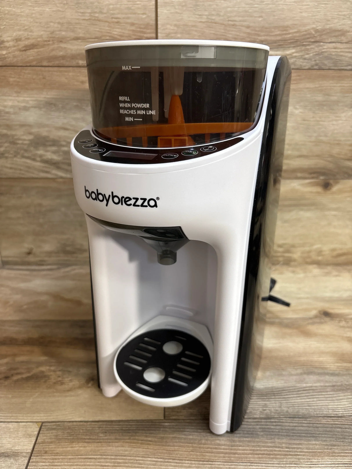 Baby Brezza formula dispenser machine on wooden floor with powder container and control buttons