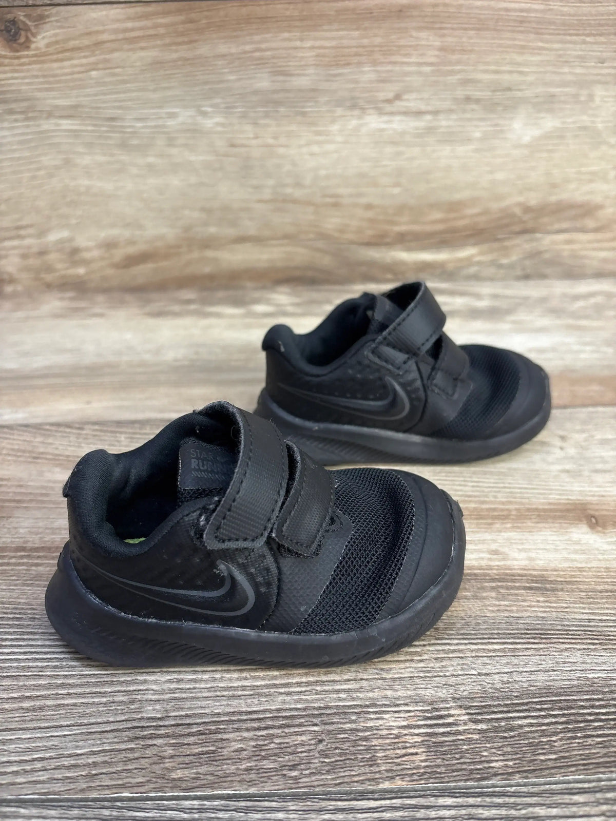Angled side view of Nike Star Runner 2 toddler sneakers showing hook-and-loop straps, mesh toe and Swoosh on wood background