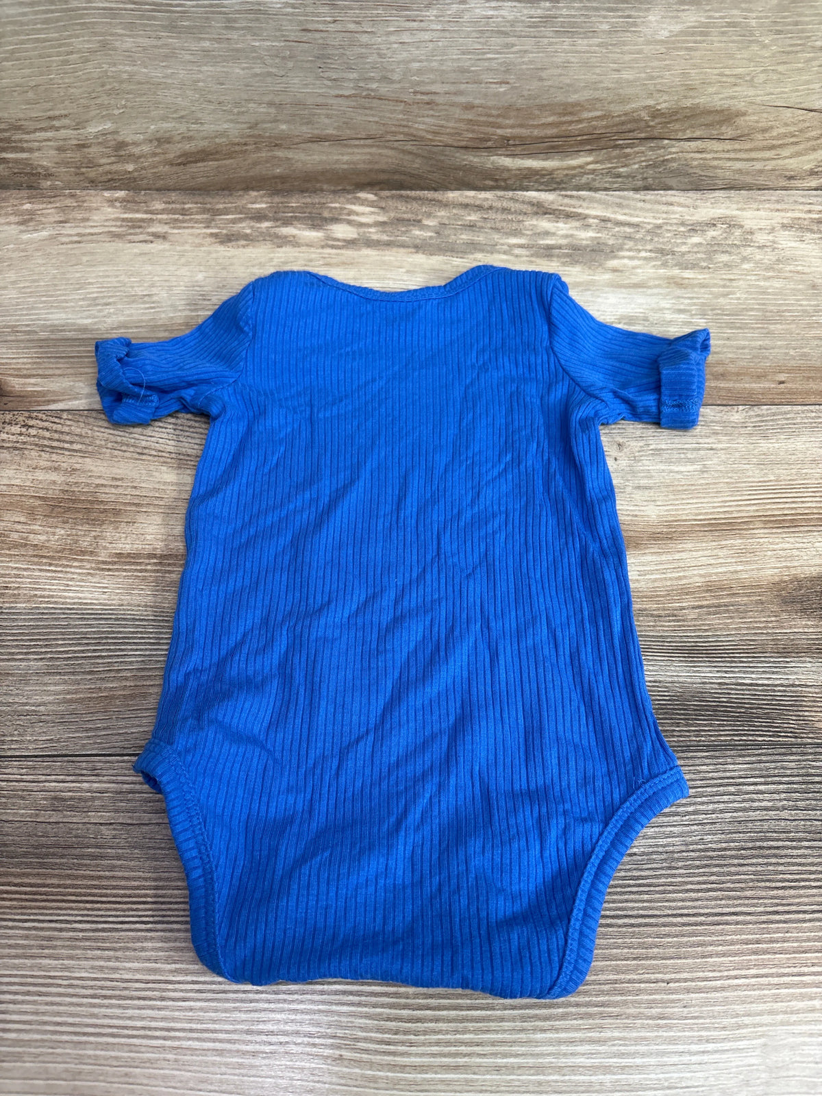 Kate Quinn ribbed modal bodysuit in blue for infants, size 3-6m, on a wood background