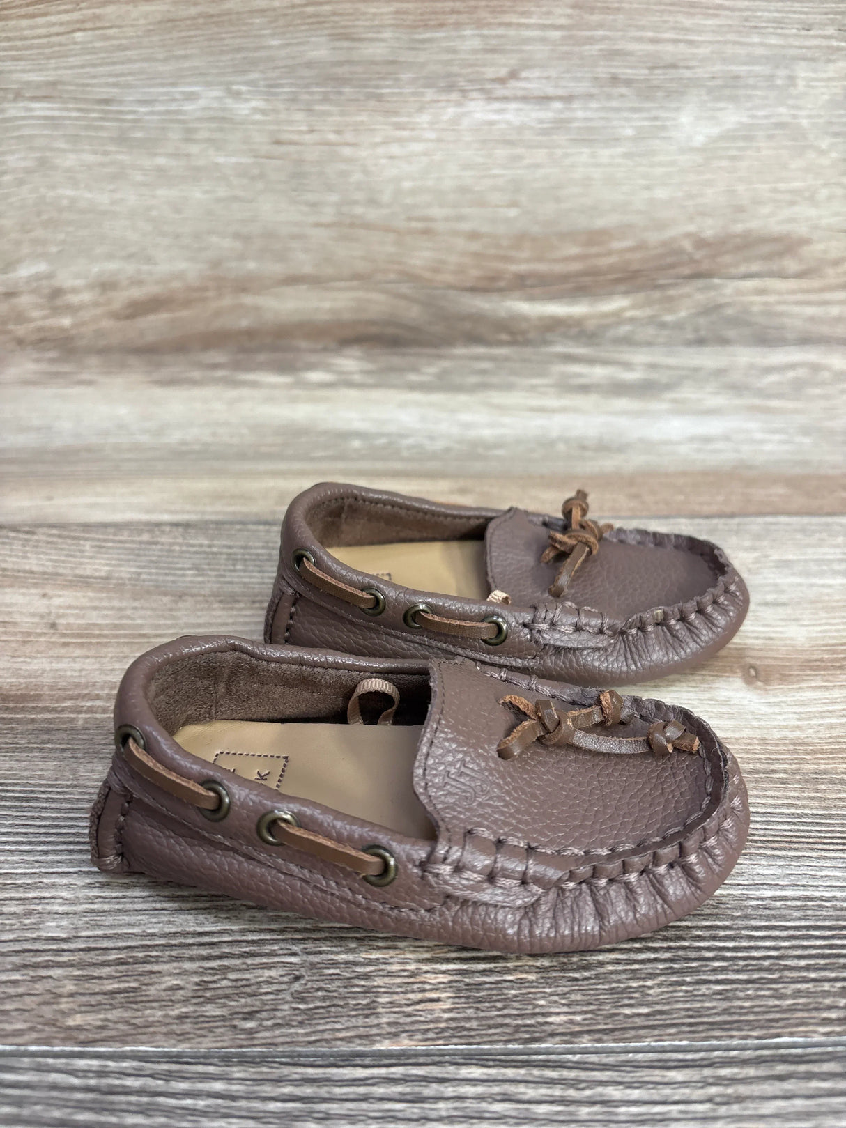 Pair of brown leather moccasin shoes with lace detailing on wooden surface