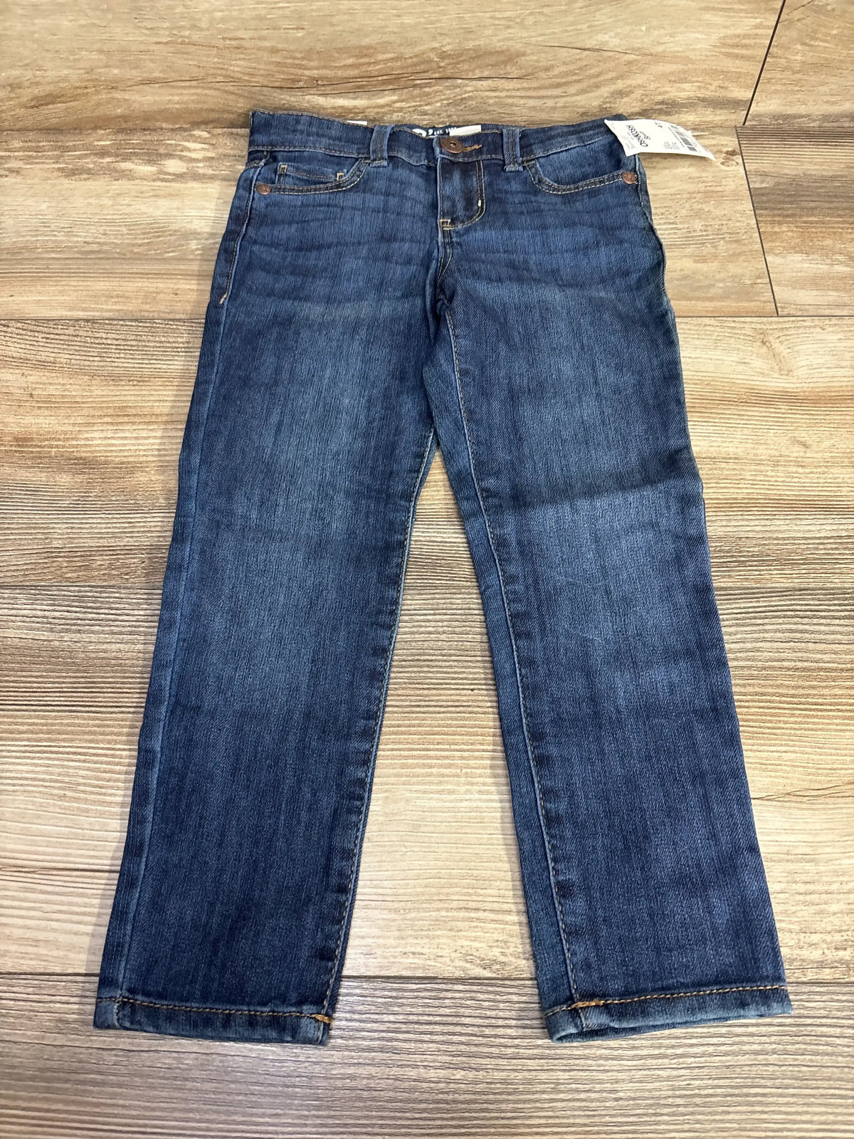 Kids blue denim jeans with front pockets and button, displayed on wood floor