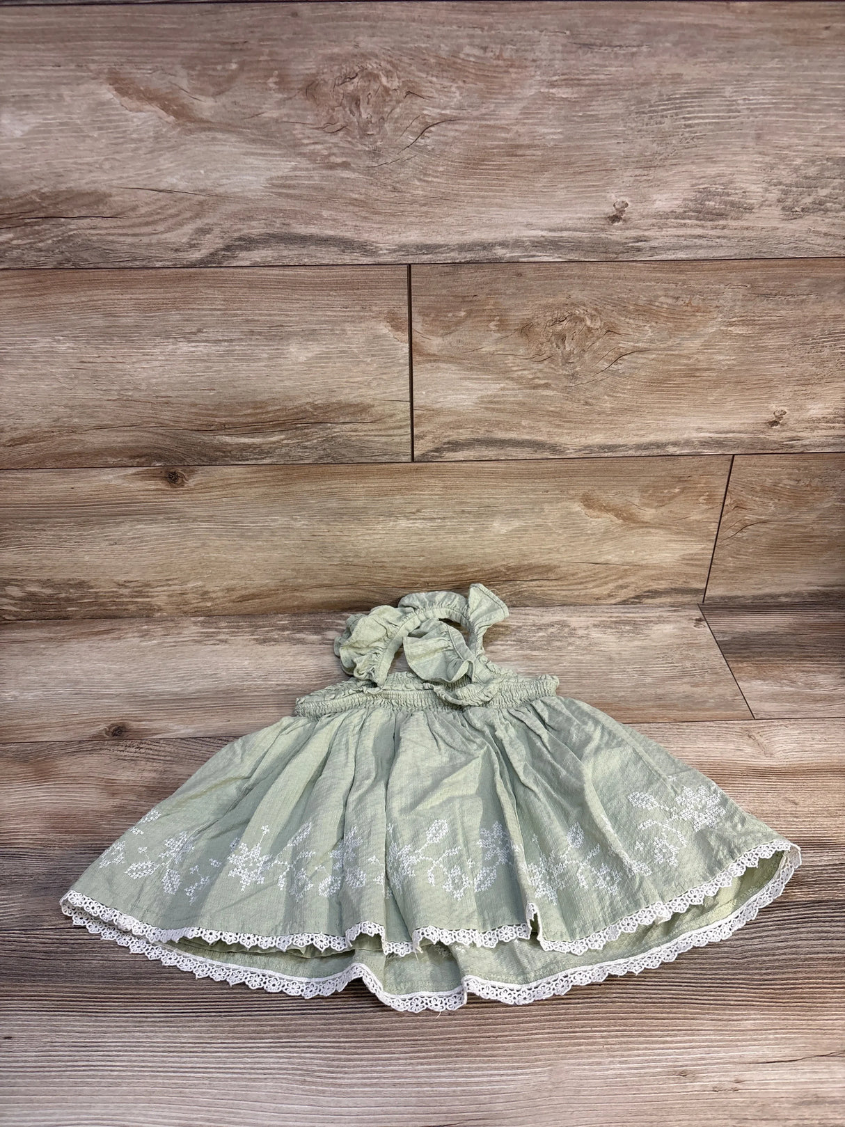 Light green baby dress with white lace trim and floral embroidery on wood background