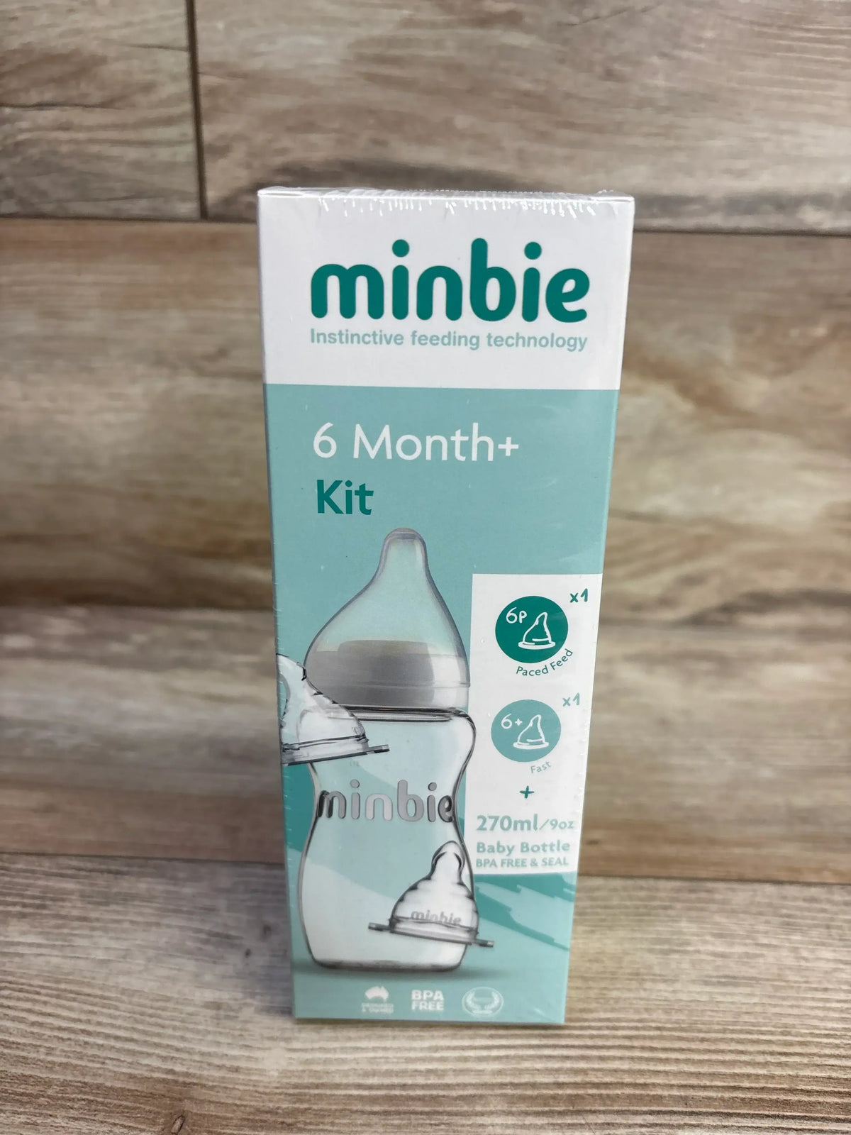 Front view of Minbie 6 Month+ feeding kit box showing 270 ml baby bottle and two teats on a wooden surface background