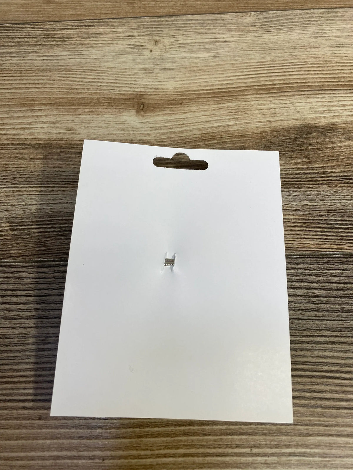 Blank white product tag with hang hole and metal clasp on wood surface