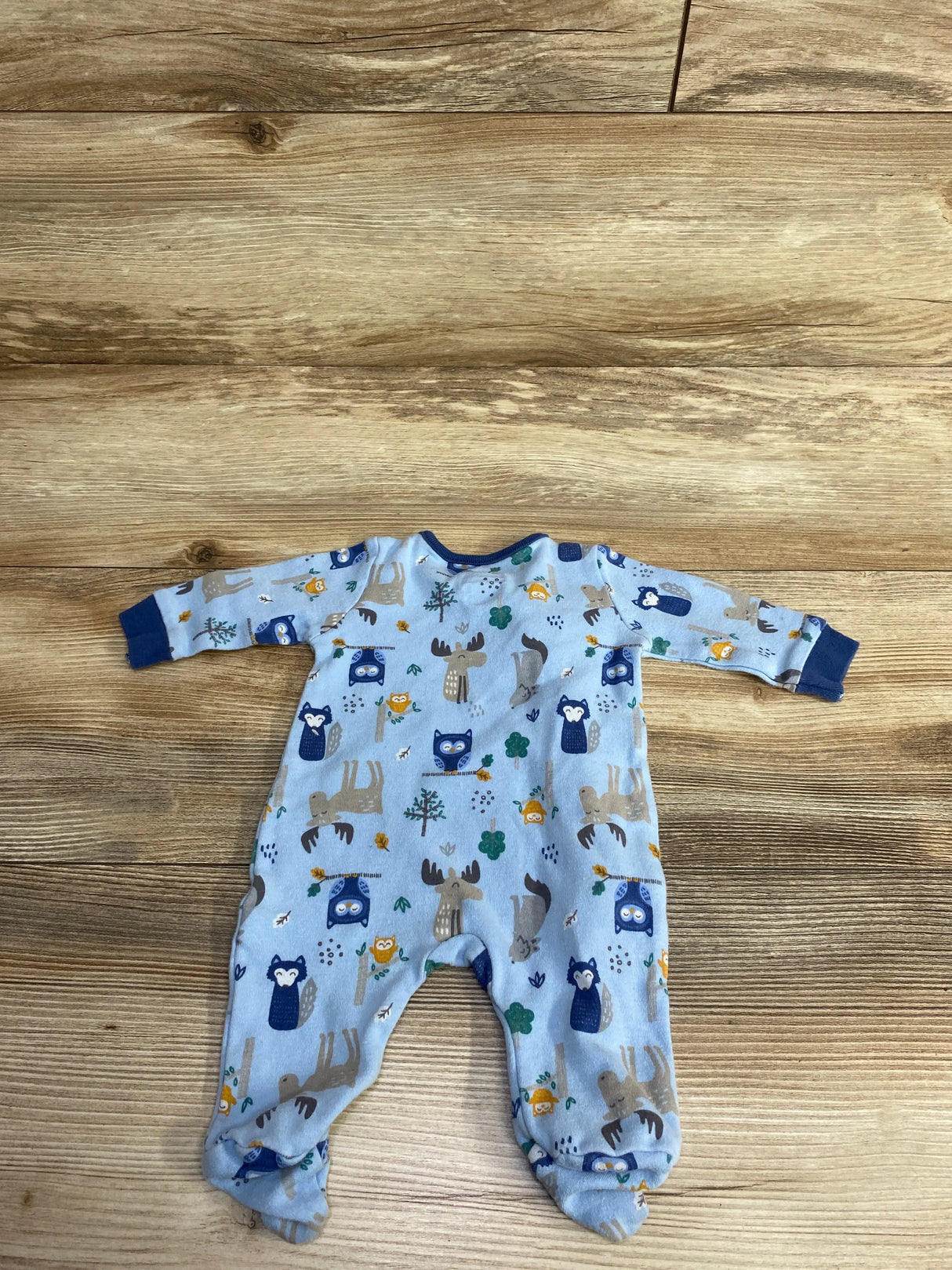 Light blue baby onesie with woodland animal prints including owls, moose, and foxes, on wooden floor