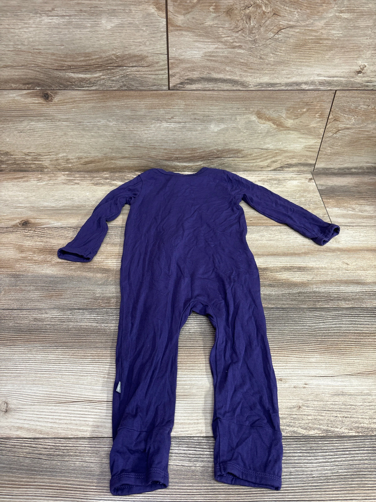 Flat lay of purple Kyte Baby bamboo footless zippered sleeper in size 18 to 24 months with long sleeves on wood grain