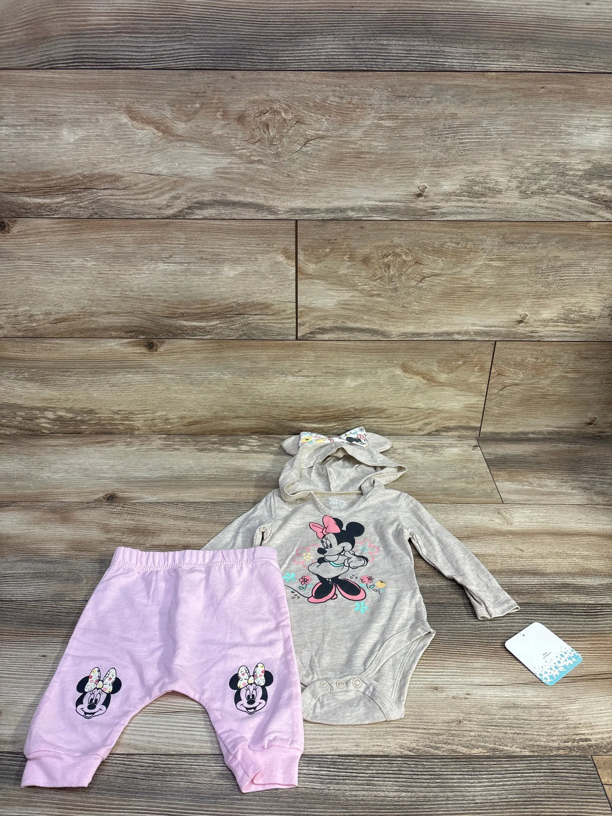 Front view of Disney Baby Minnie Mouse two-piece set with hooded long-sleeve bodysuit and matching pants on wood