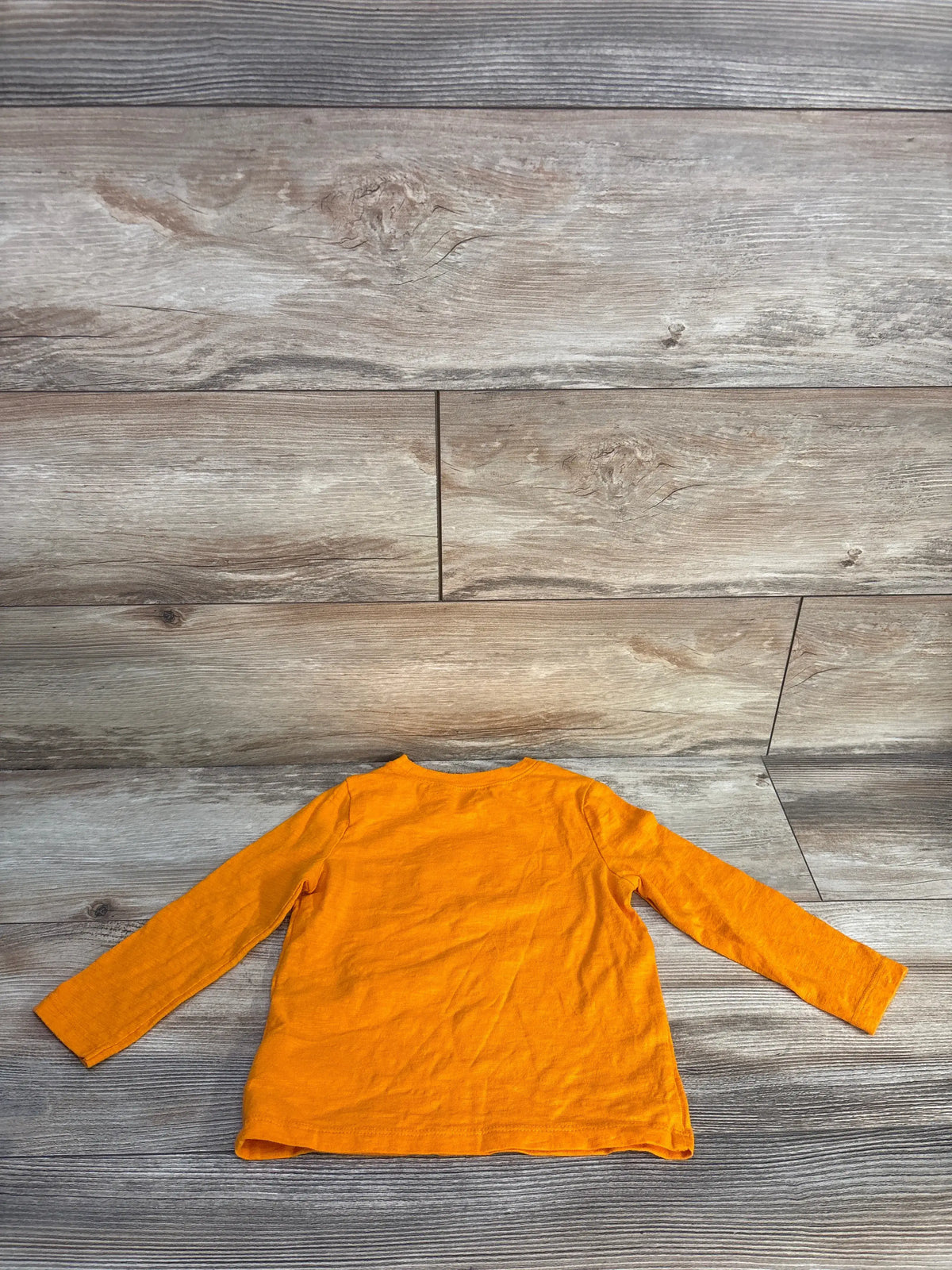 Back view of Old Navy Got Candy Halloween shirt showcasing orange long sleeves with a wood look background